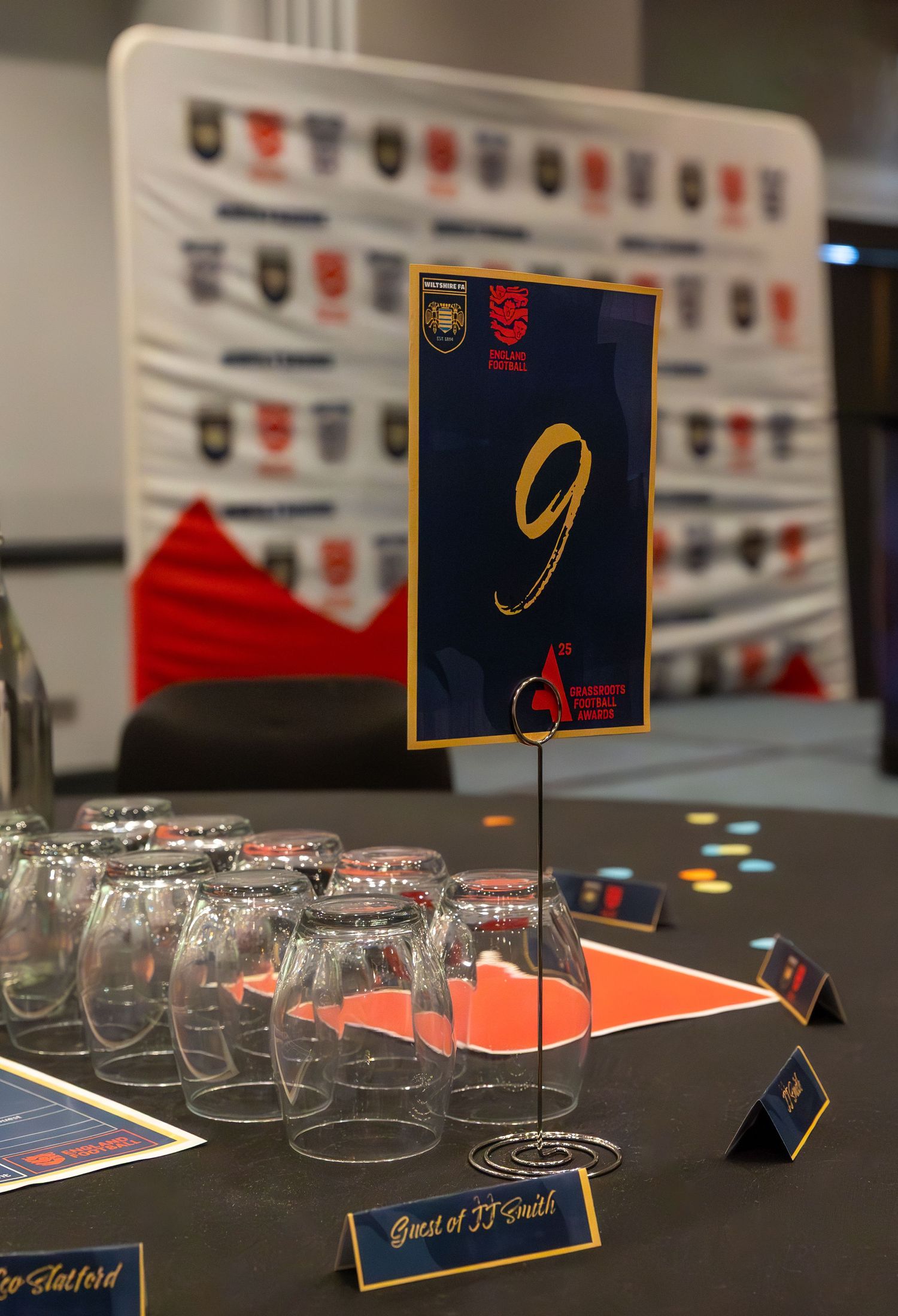 Event setup with wine glasses and name cards displayed on a black surface with decorative badges on the wall.