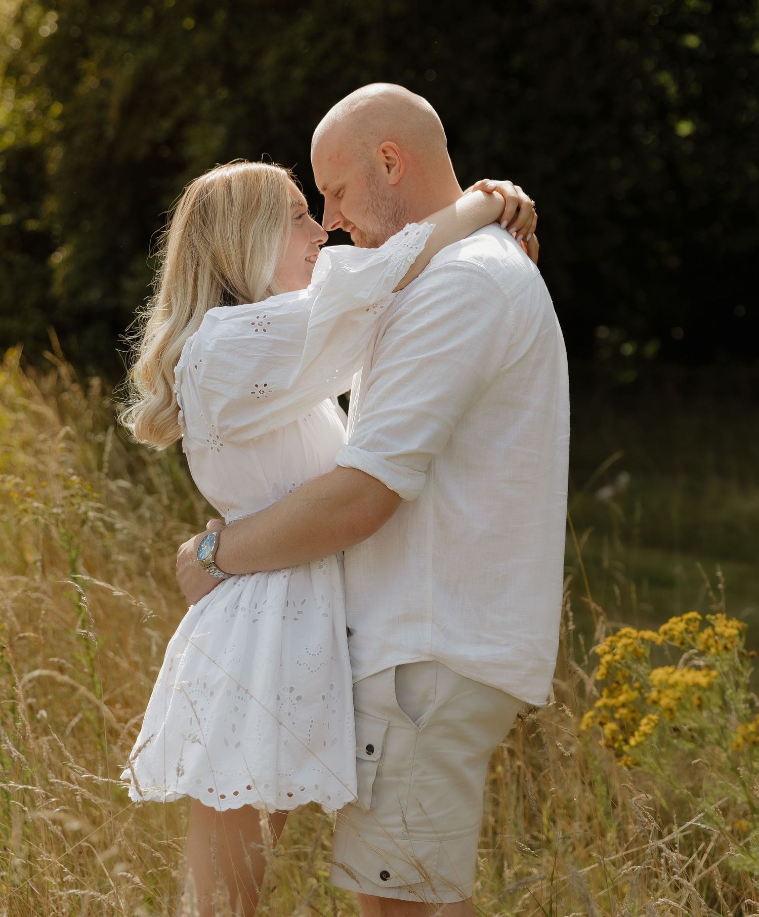 A couple embracing in a sunny field wearing coordinated white summer outfits.