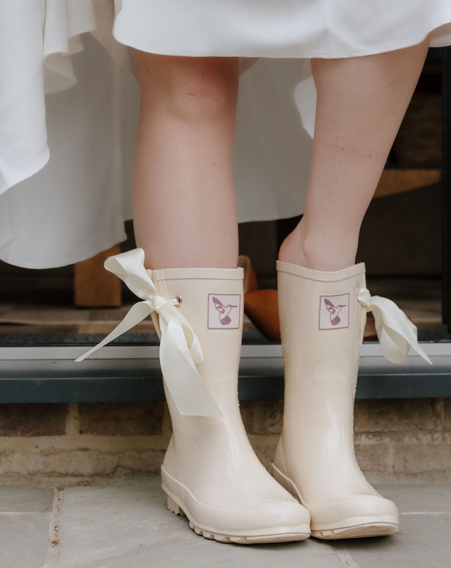 White rain boots with ribbon laces shown against concrete background.