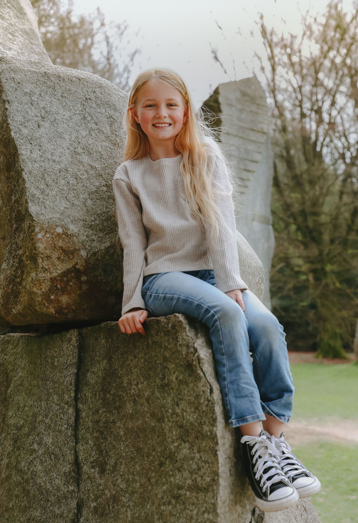 Child in casual outfit sitting on stone wall outdoors with natural backdrop.