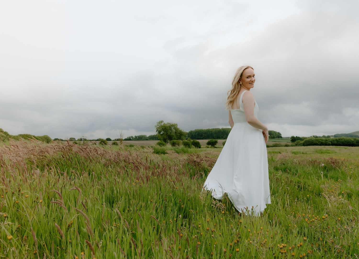 White dress twirls through tall grass in a dreamy countryside landscape.