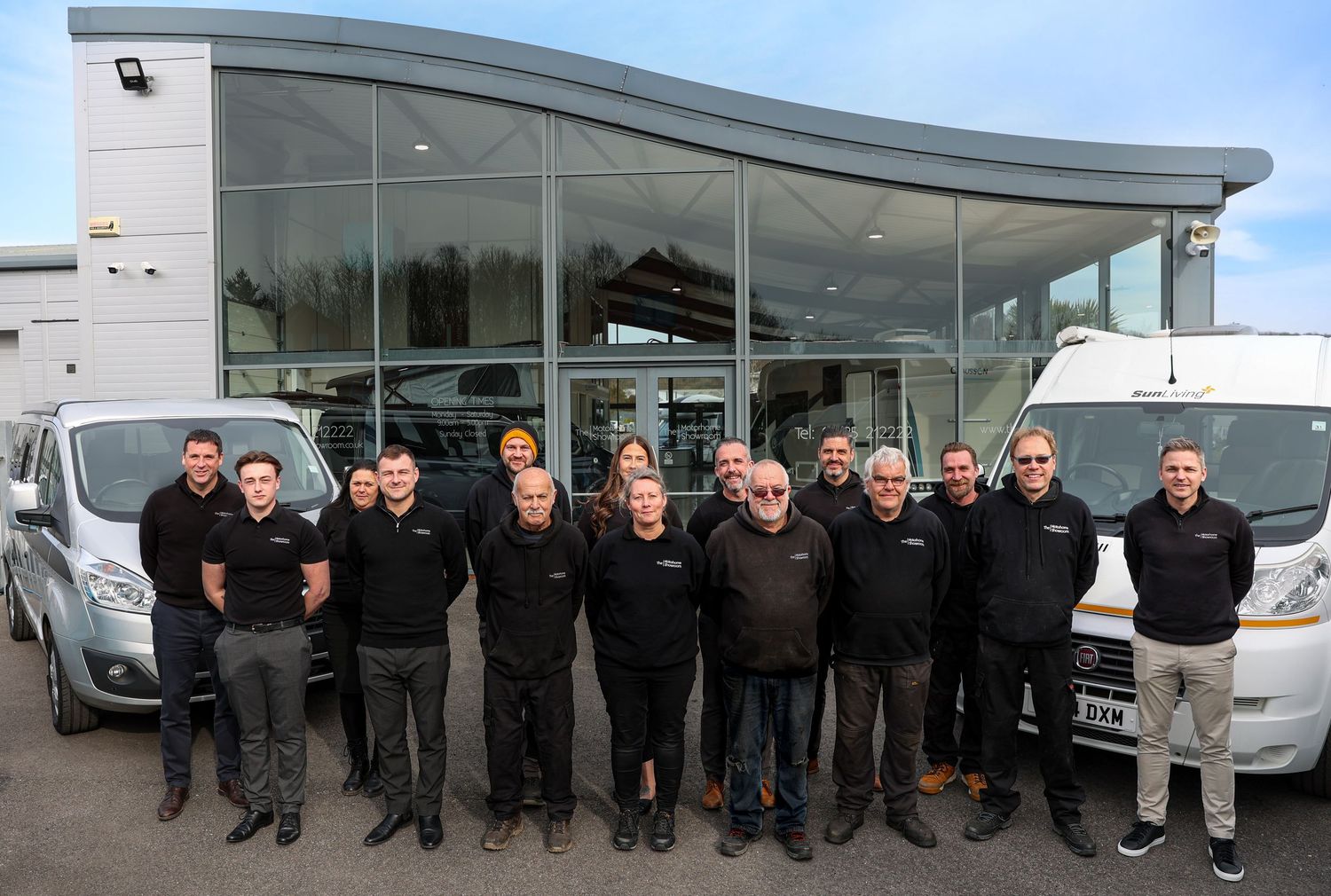 Team of automotive professionals standing in front of luxury car dealership.