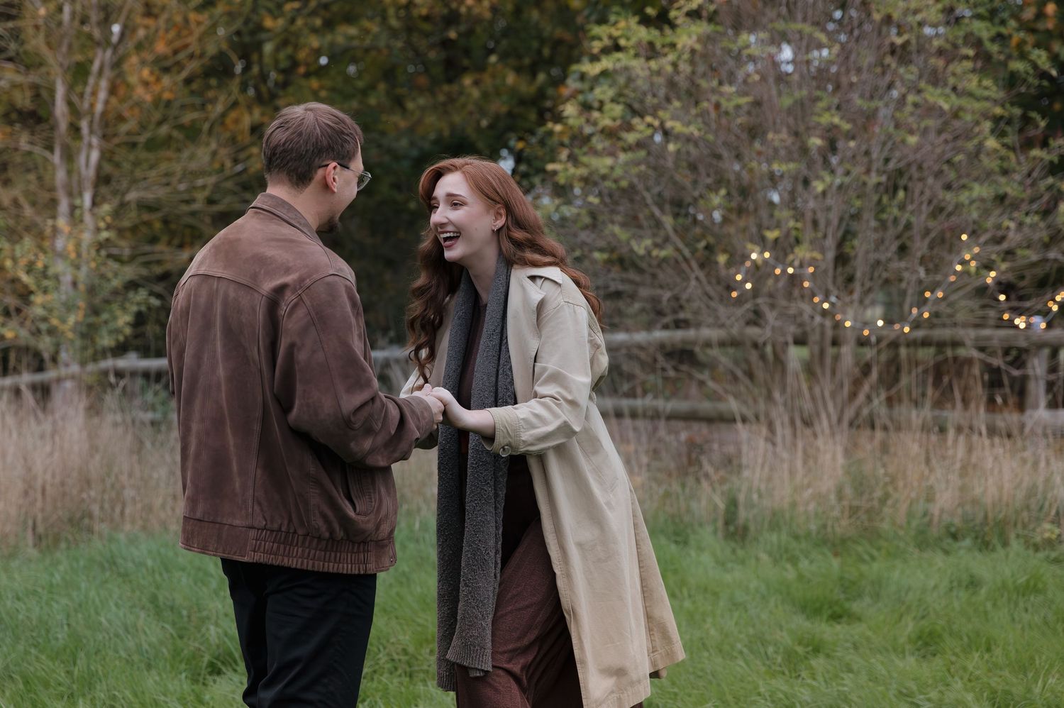 Two people share a joyful moment while standing in a grassy field on an autumn day.