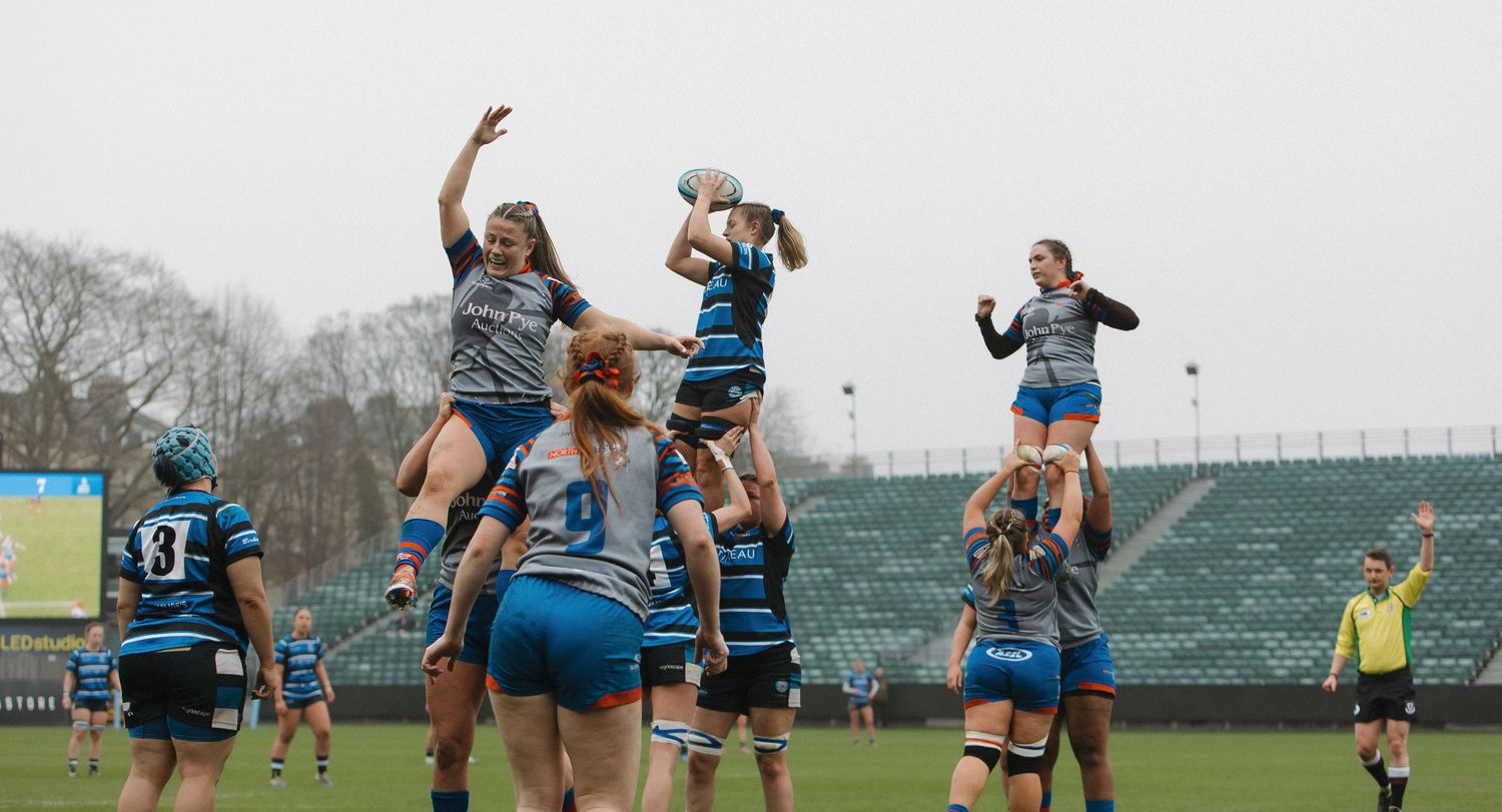 Rugby players leap high in the air to catch the ball during a lineout play on a cloudy day.