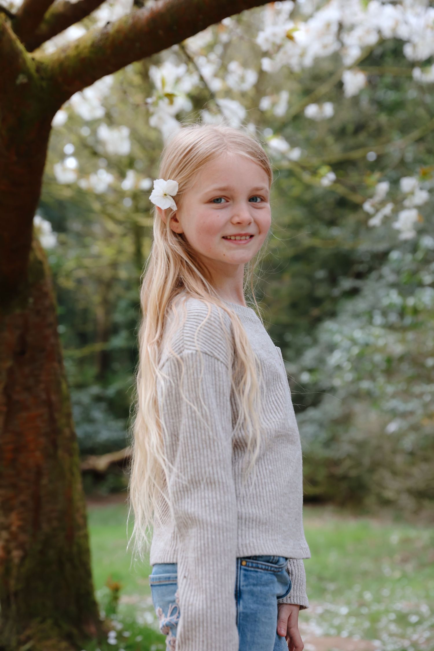 Young person in striped sweater standing beneath flowering tree branches in springtime.