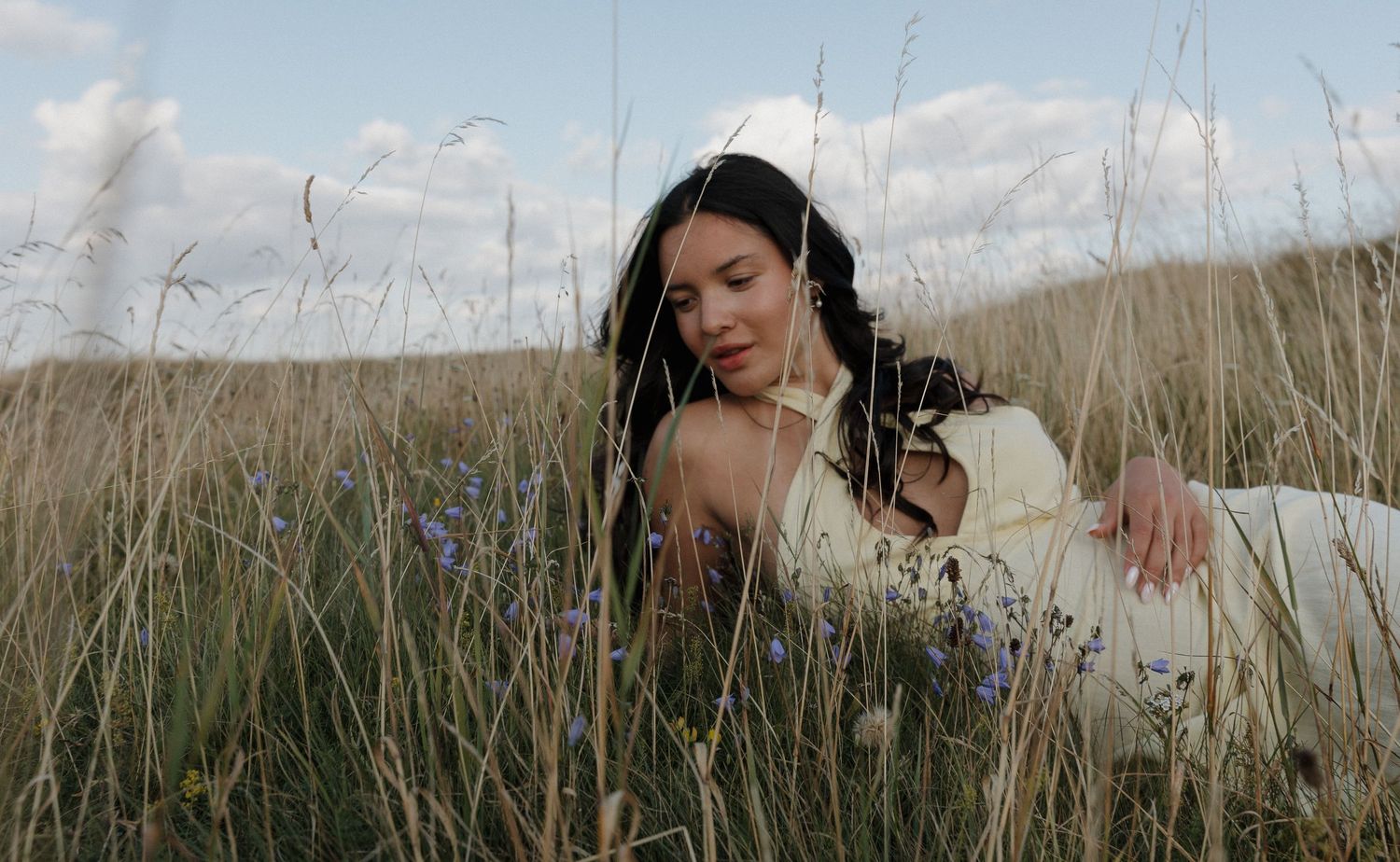 Artistic photo of someone sitting in tall grass against cloudy sky.