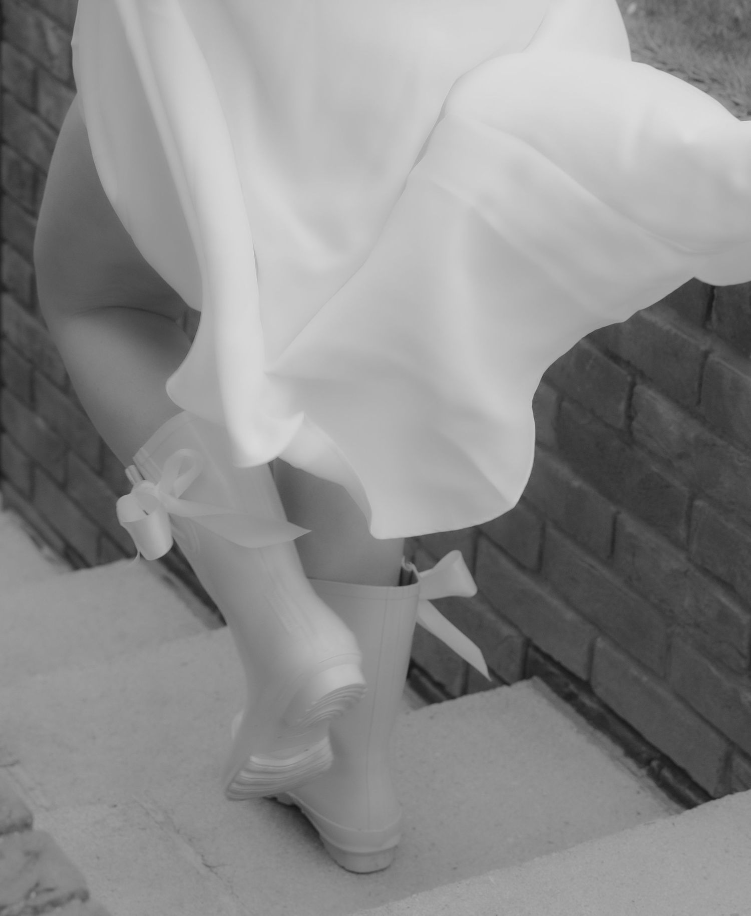 White flowing dress hem and shoes against a dark brick wall background.