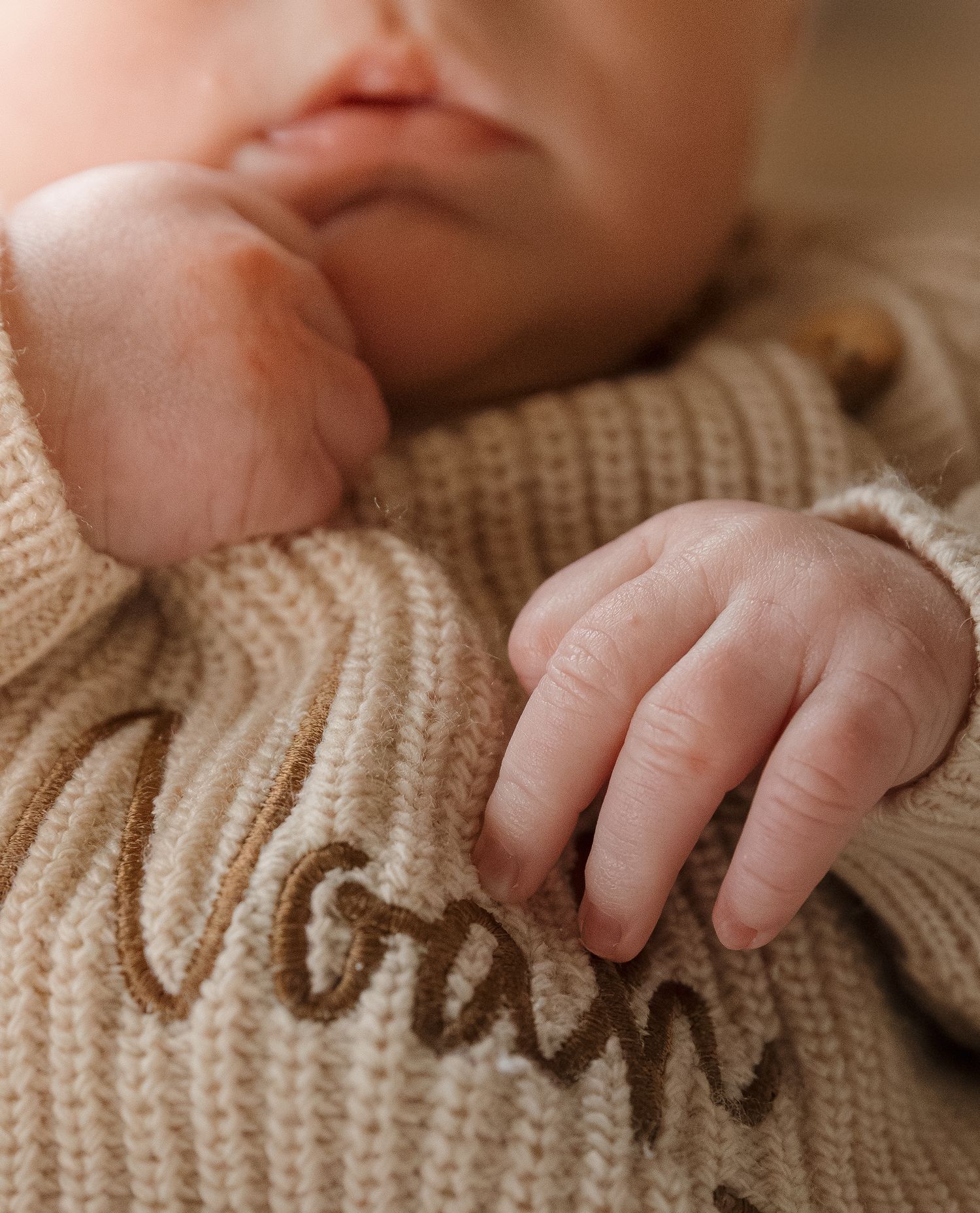 Close-up macro shots of tiny baby hands grasping a soft knit cream-colored fabric.