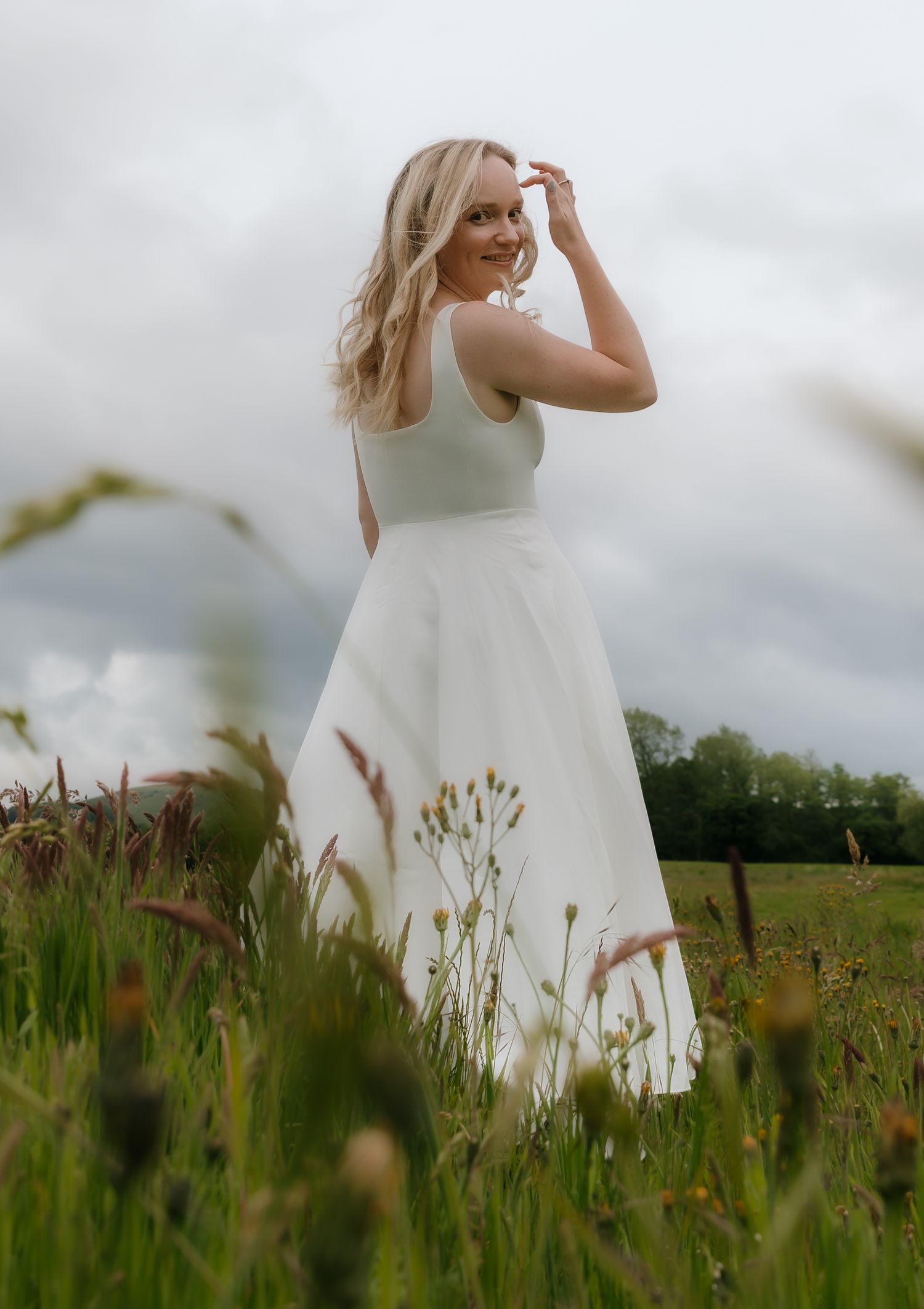A white dress flows elegantly through a green summer meadow on a cloudy day.