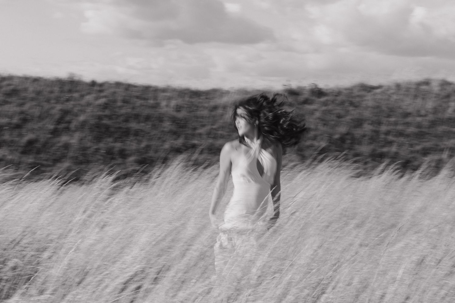 Artistic black and white portrait of woman in dress standing in windswept field.