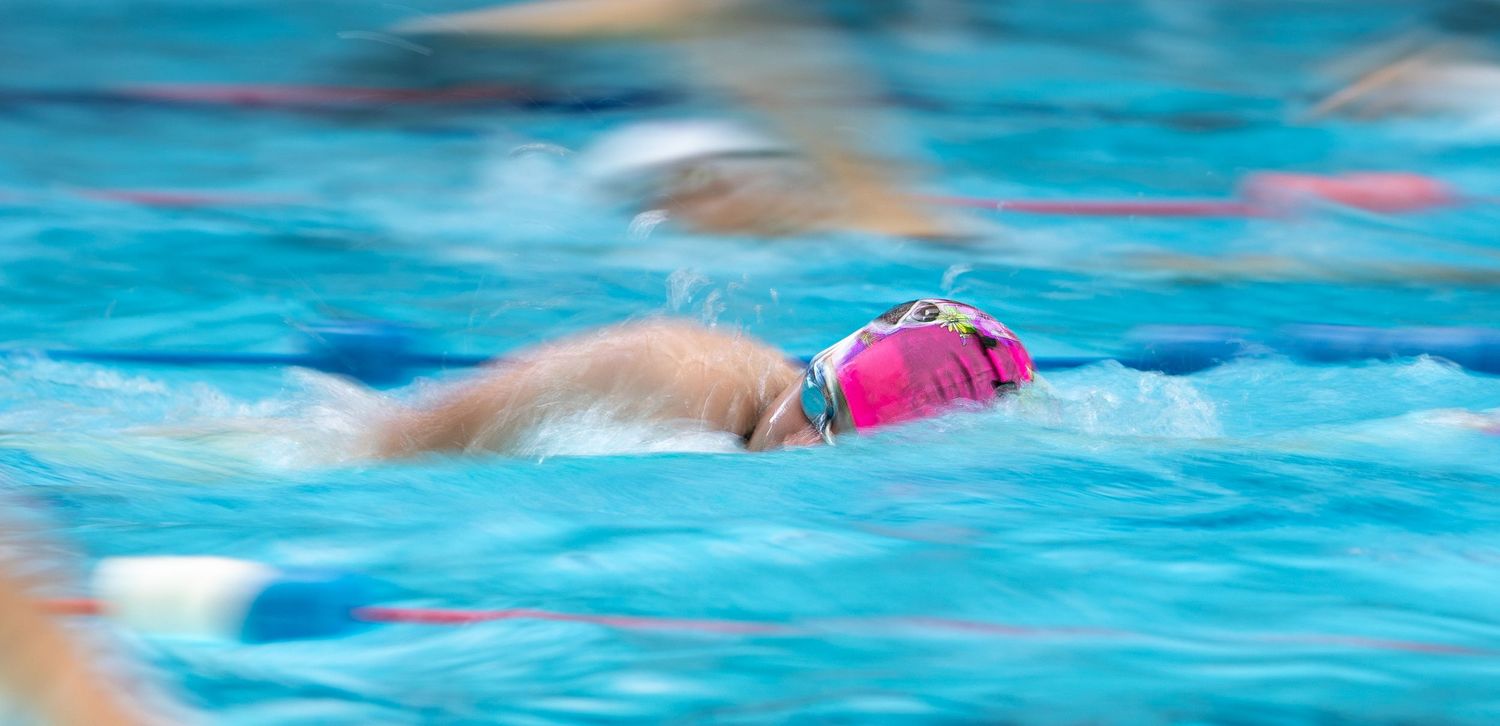 Abstract motion blur of swimmers moving through blue pool water.