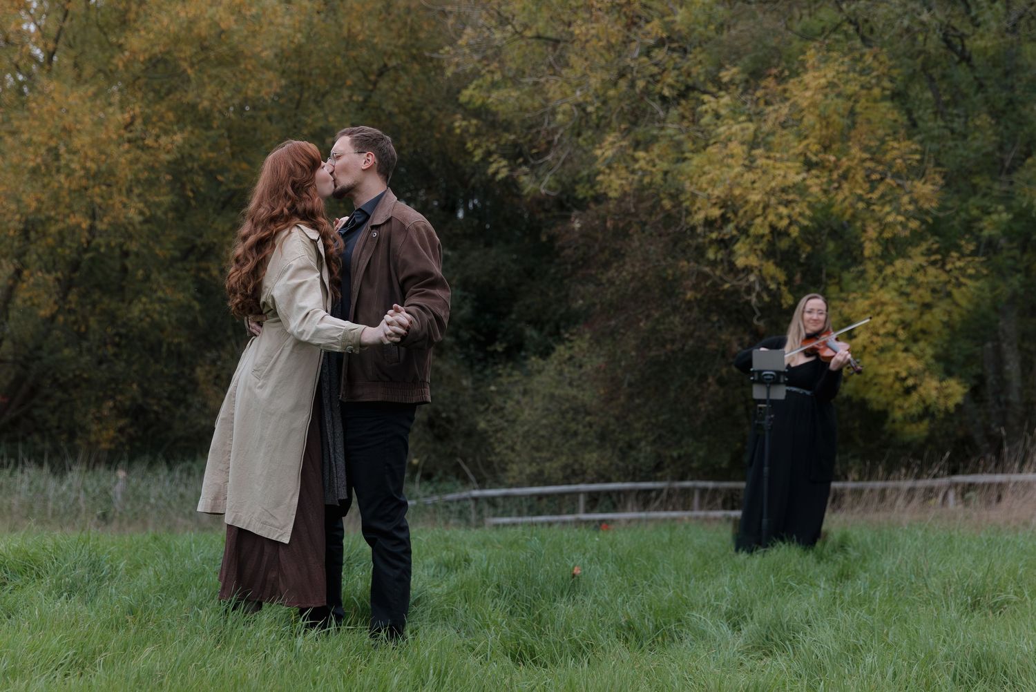 A couple shares an intimate moment in a rustic outdoor setting surrounded by autumn foliage.