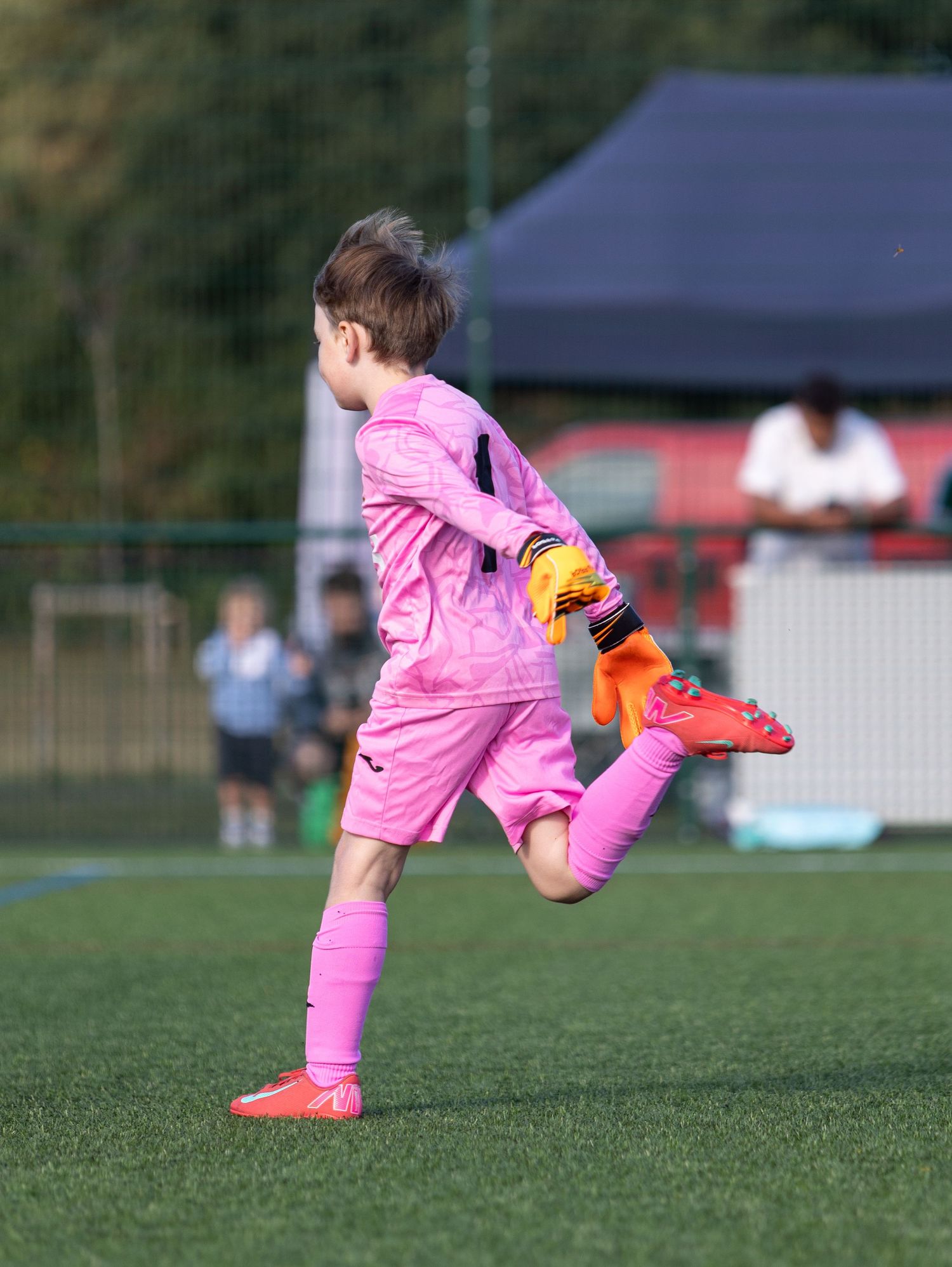 Soccer goalkeeper in pink uniform practices diving saves on grass field during training session.