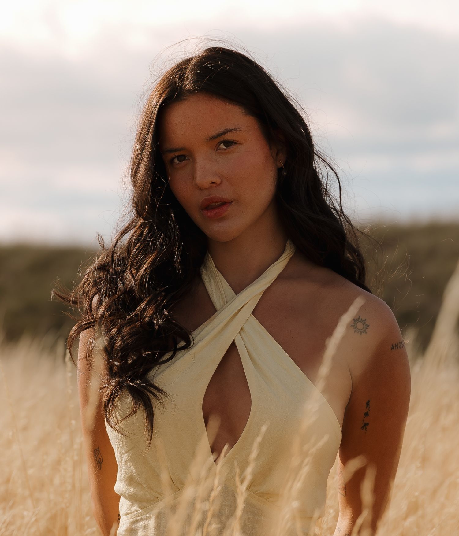 Portrait of a model in a white halter dress amid a golden field during sunset.