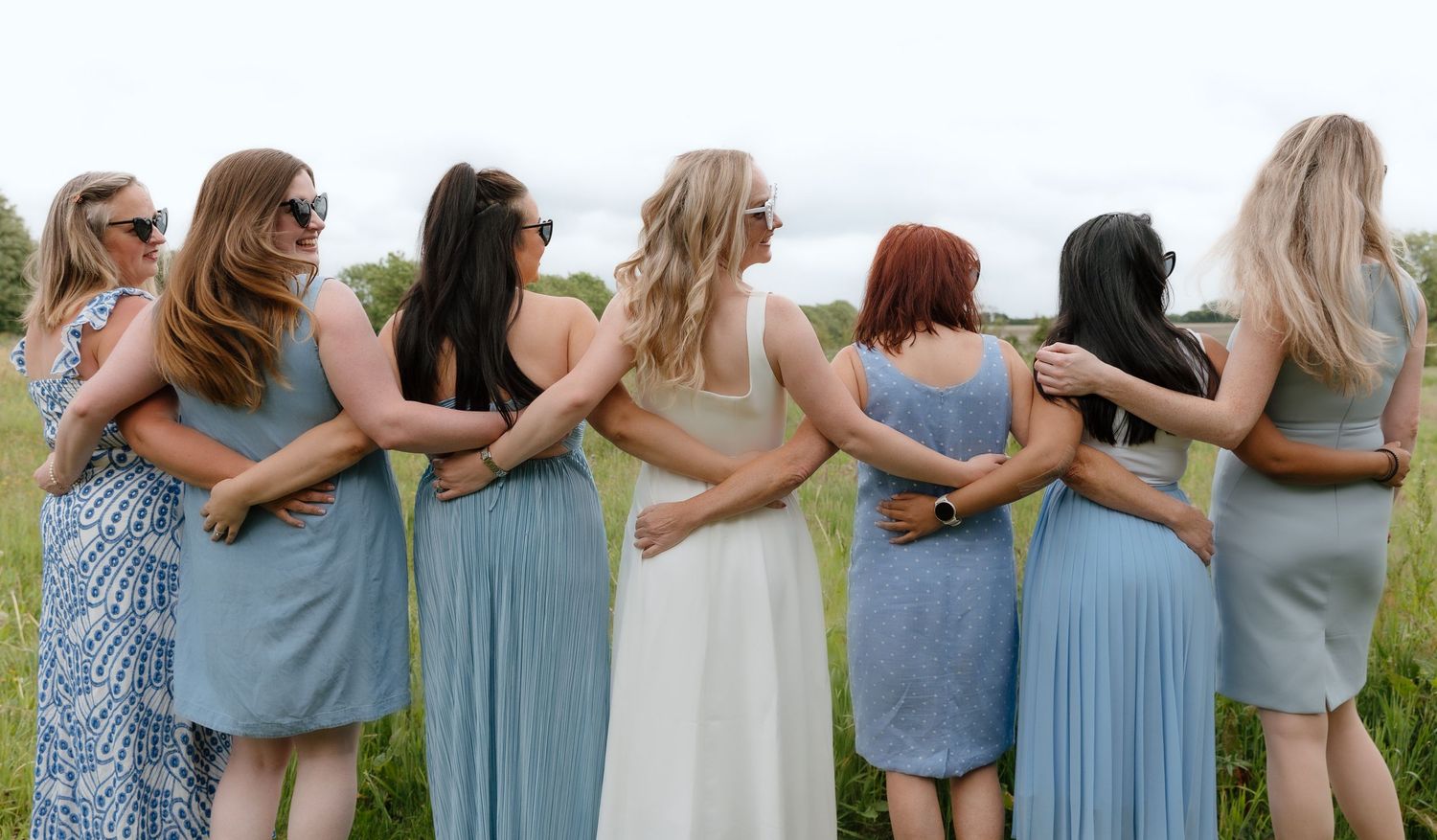 Group of women in matching light blue dresses standing arm-in-arm outdoors.