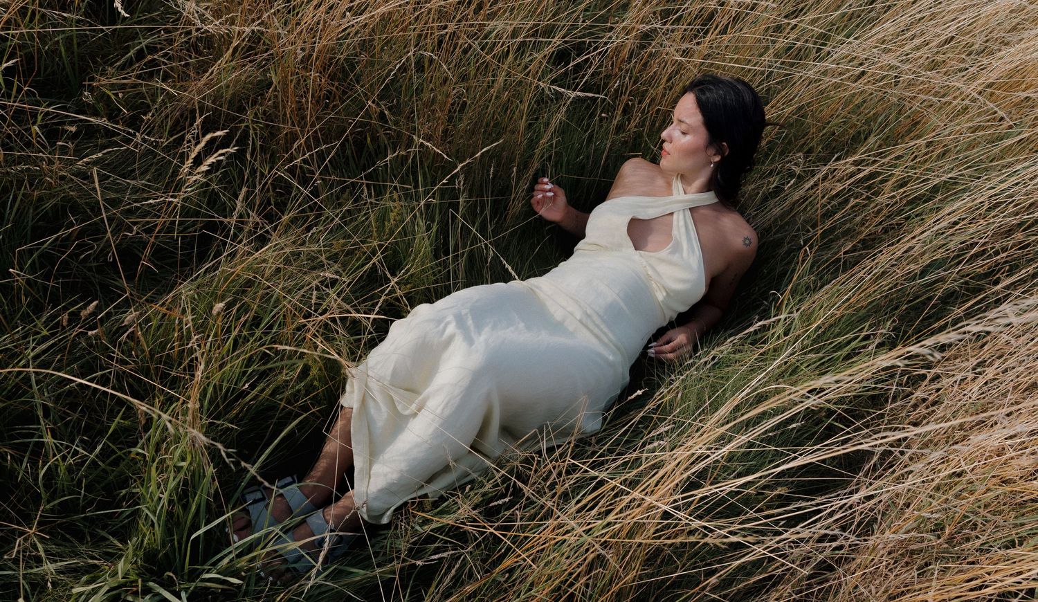Person in white clothing lying in tall golden grass during sunset.