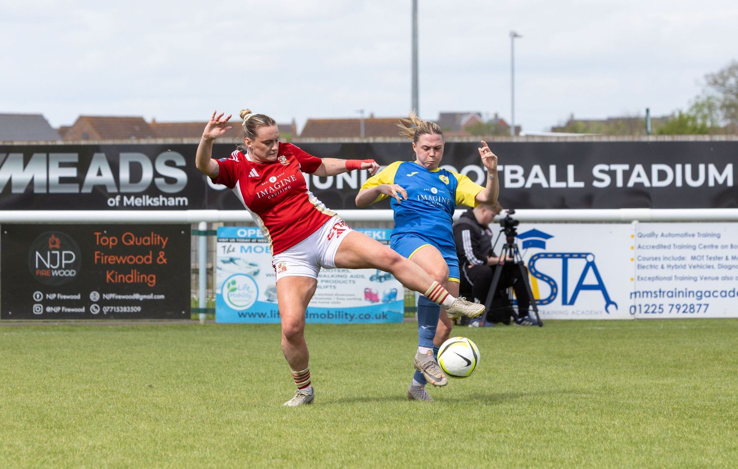 Two women soccer players compete for the ball during a match at Melksham football stadium.