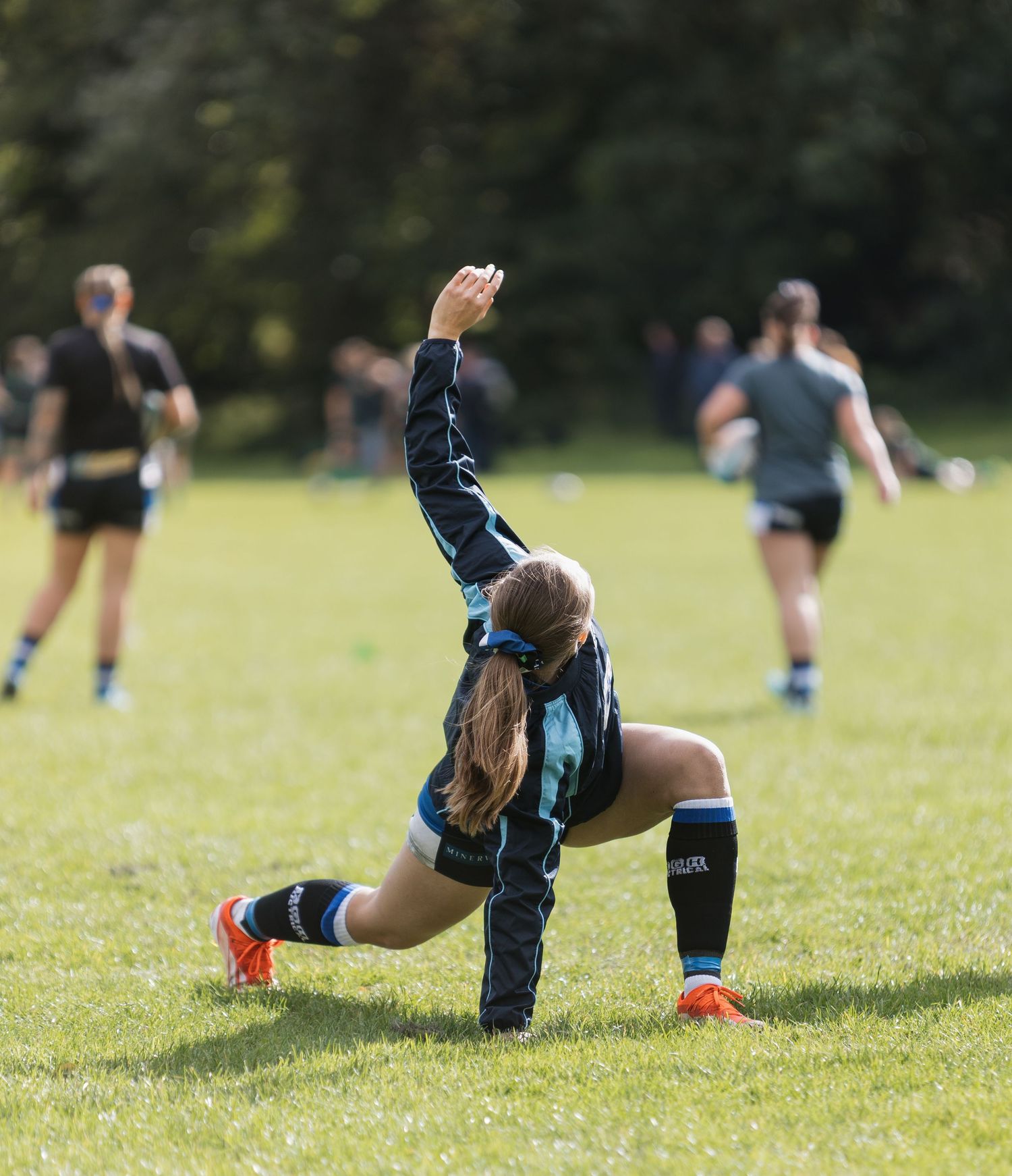 Bath rugby players practicing sliding drills on a grassy field during a sunny day training session.