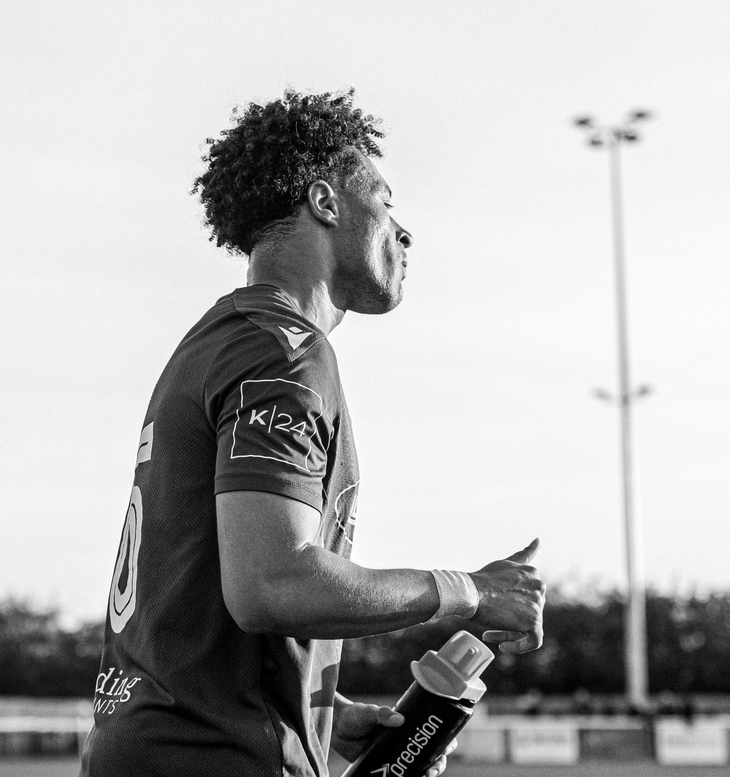 Black and white photo of a male athlete in sports jersey holding a water bottle on a sports field.