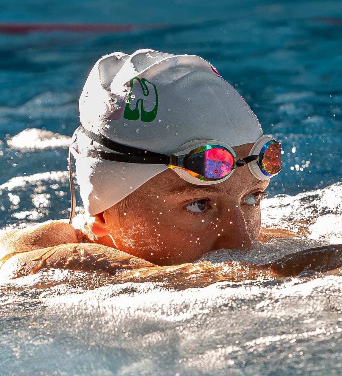 Close-up of competitive swimmers in white caps gliding through blue water.
