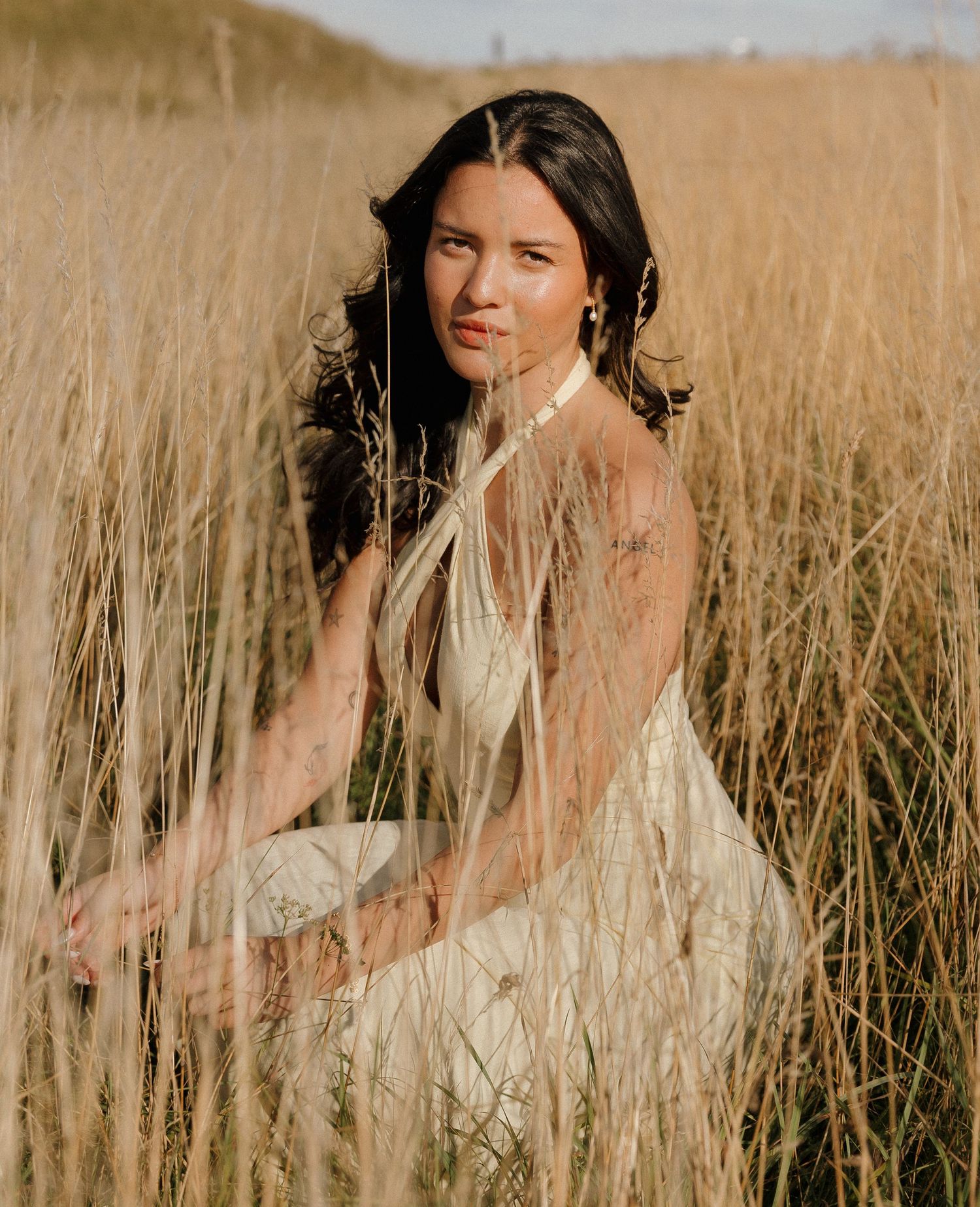 Person in white dress sitting among tall golden grass during sunset.