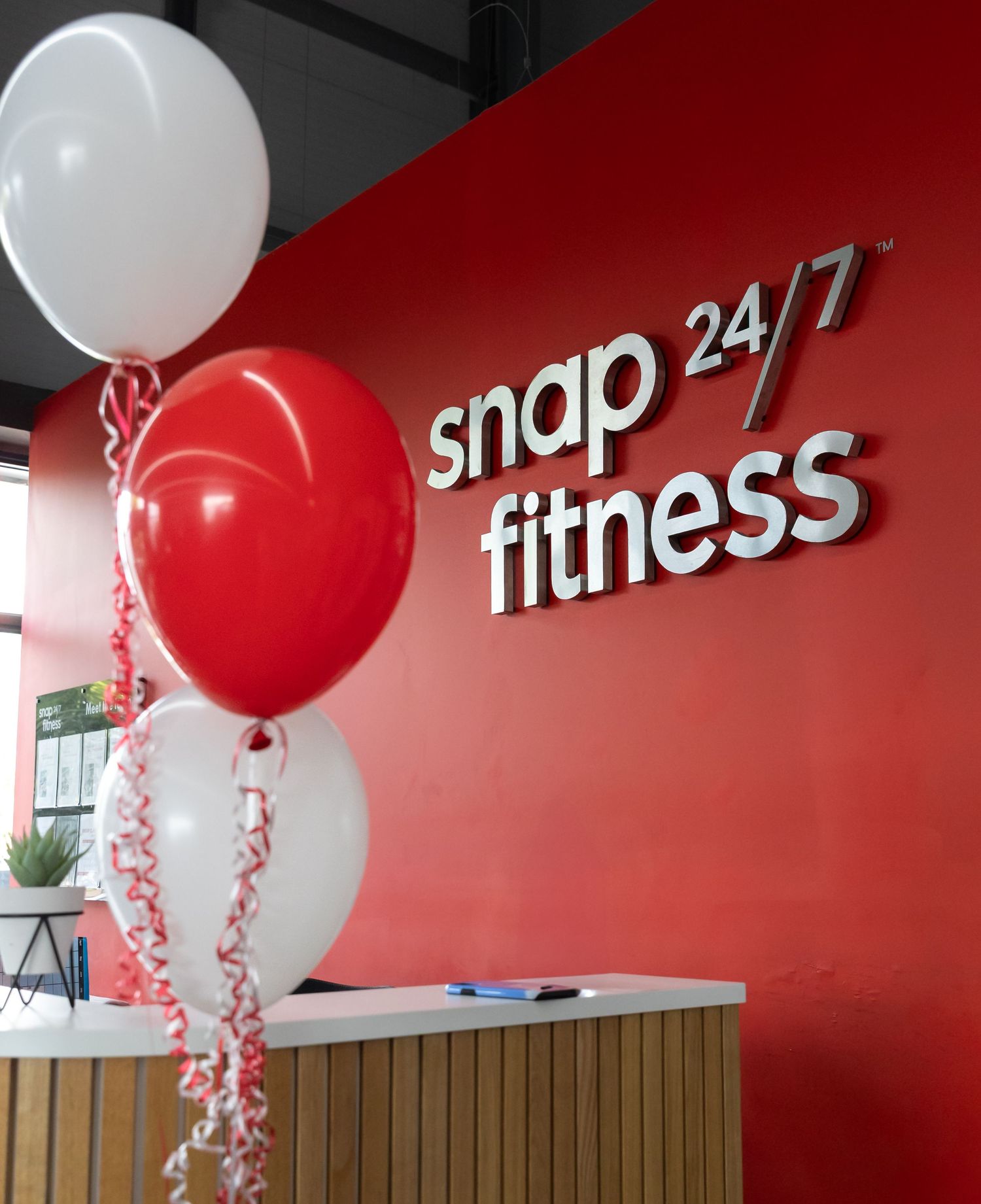 Snap Fitness 24/7 logo on red wall with festive red and white balloons for decoration.