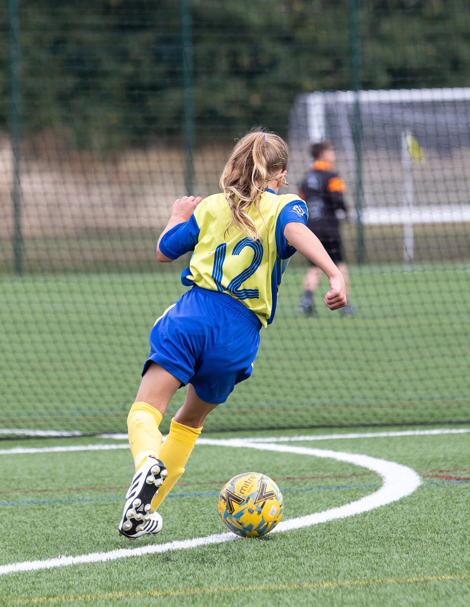Soccer player in yellow and blue uniform performs sliding tackle during match on grass field.