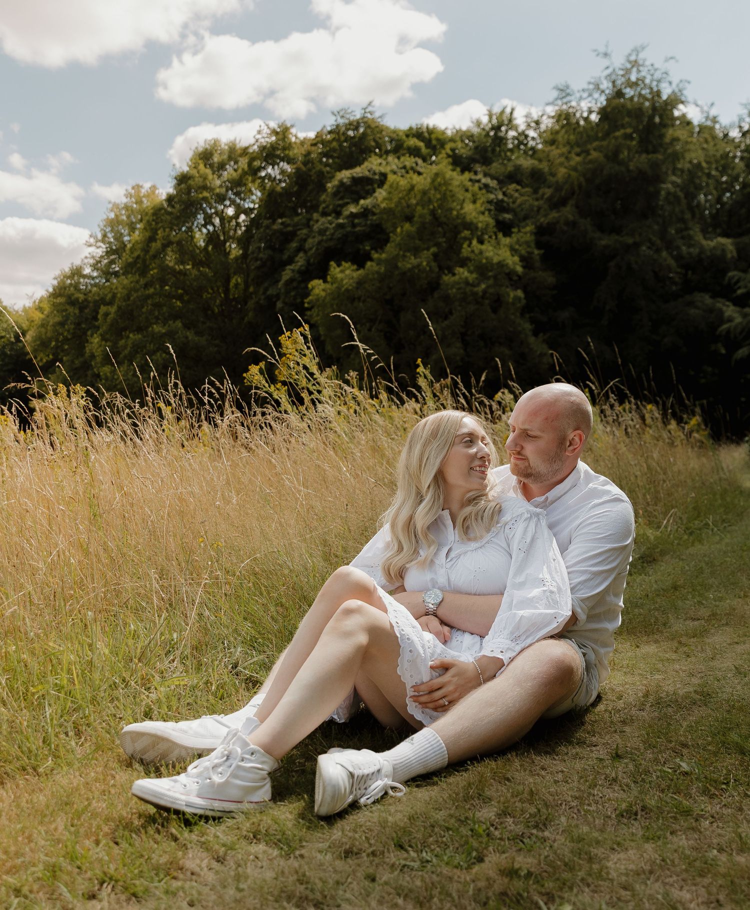 Romantic couple in white clothing lounging together in a sun-drenched meadow of tall grass.