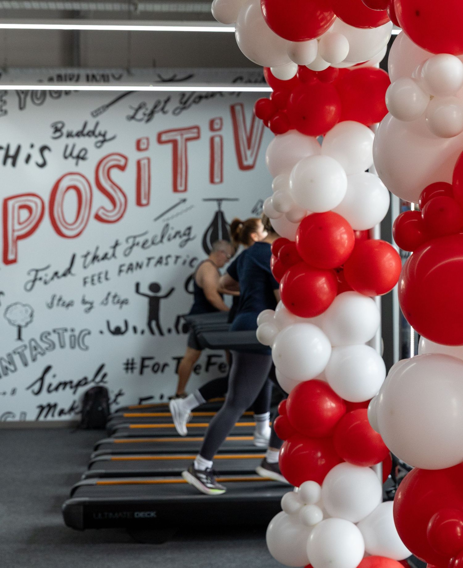 Person running on treadmill with motivational wall art and red and white balloon arch.