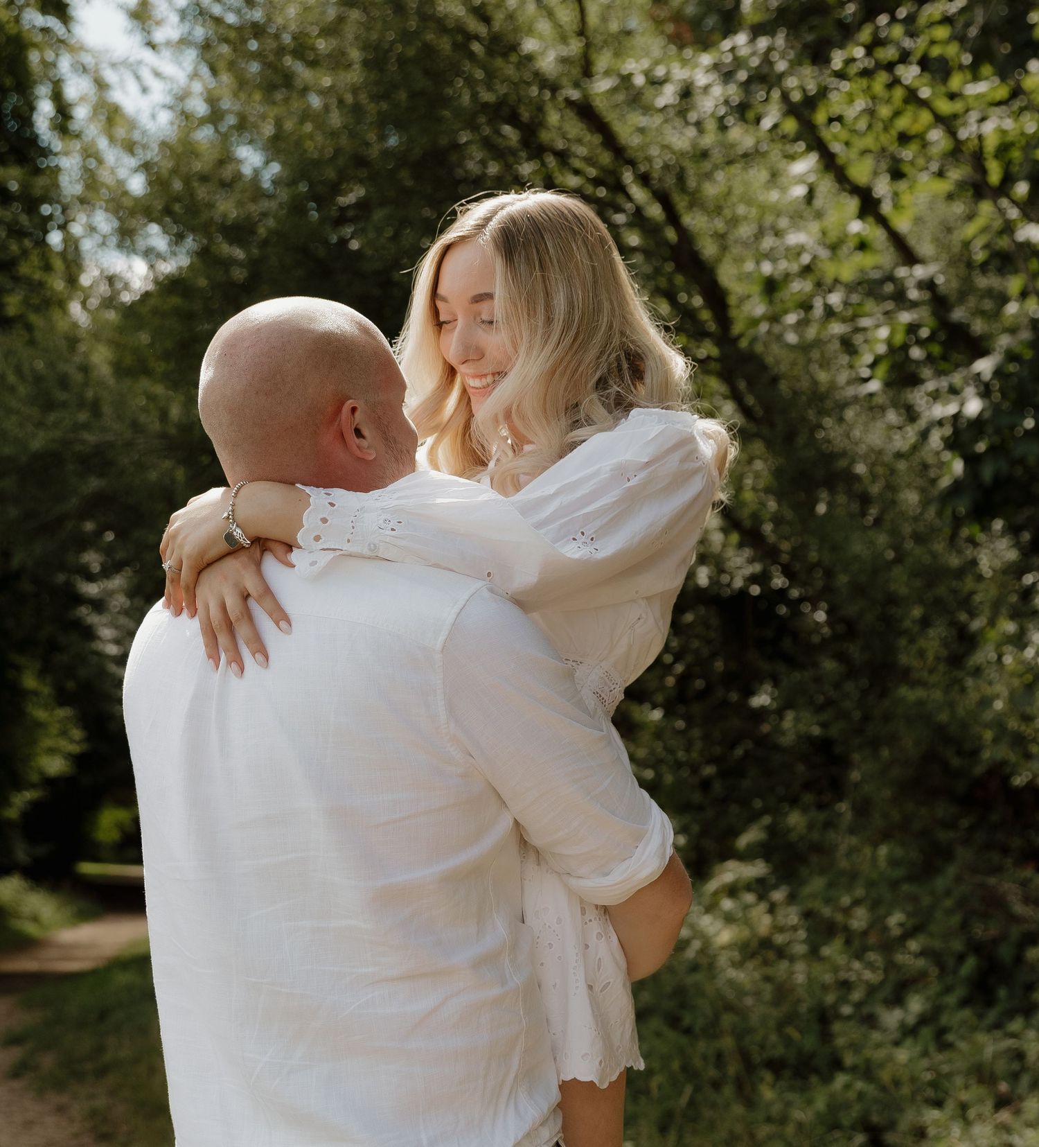 An intimate moment captured between a couple in white clothing surrounded by lush greenery.