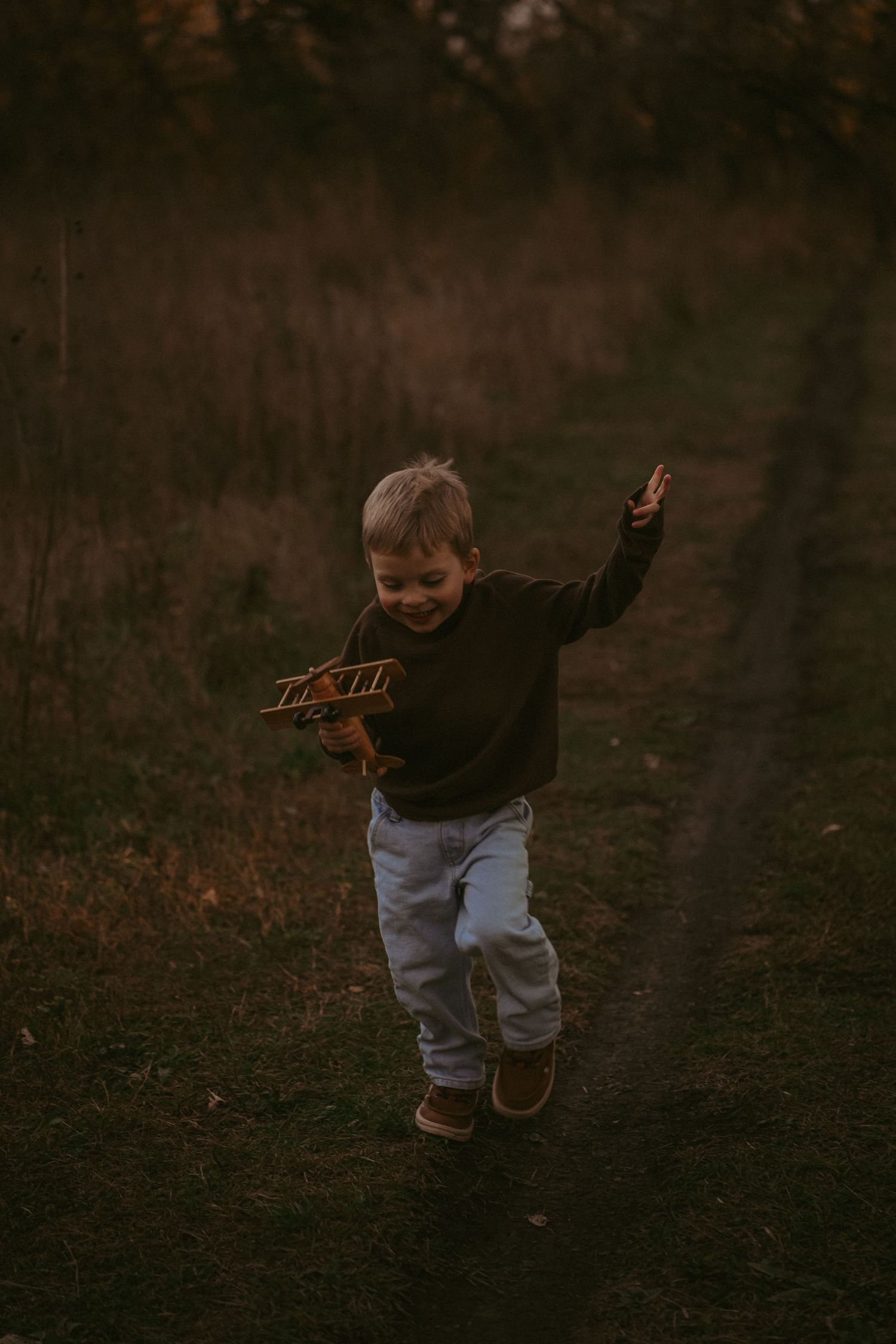Young child jumps playfully on an outdoor path at dusk.
