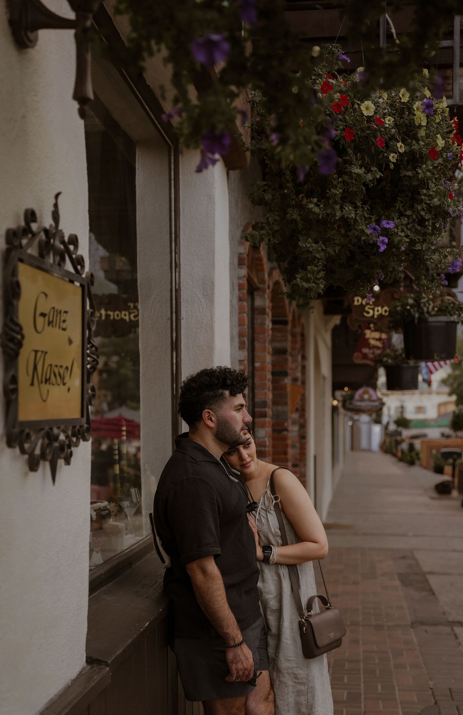 Couple walking together along a charming storefront with hanging flower baskets.