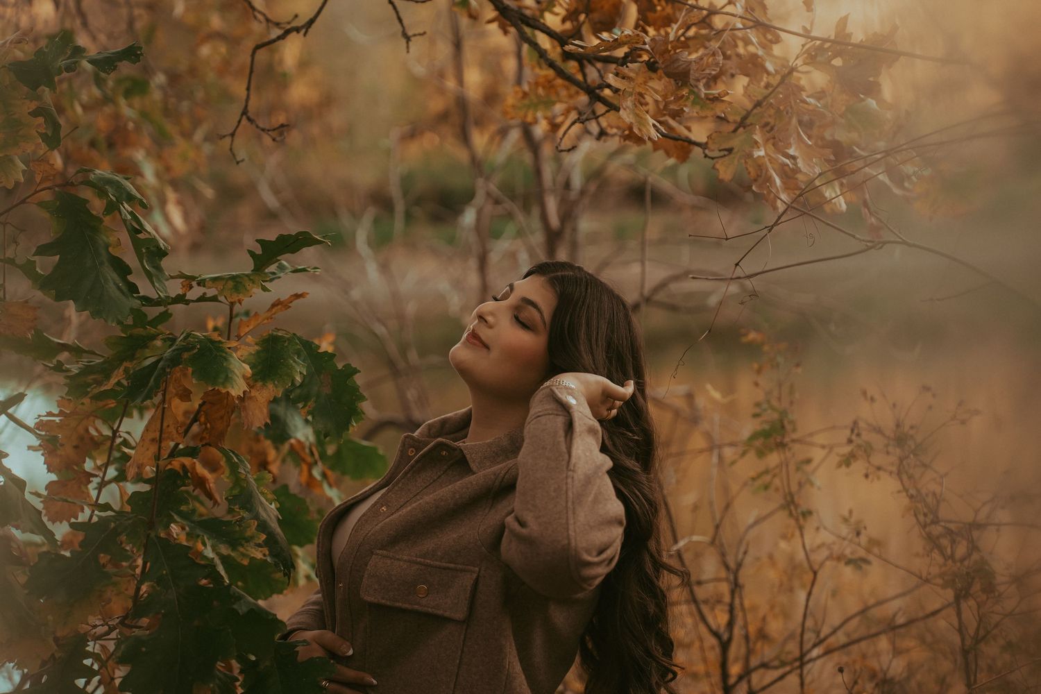 A dreamy autumn portrait session in a forest with soft golden light filtering through falling leaves.