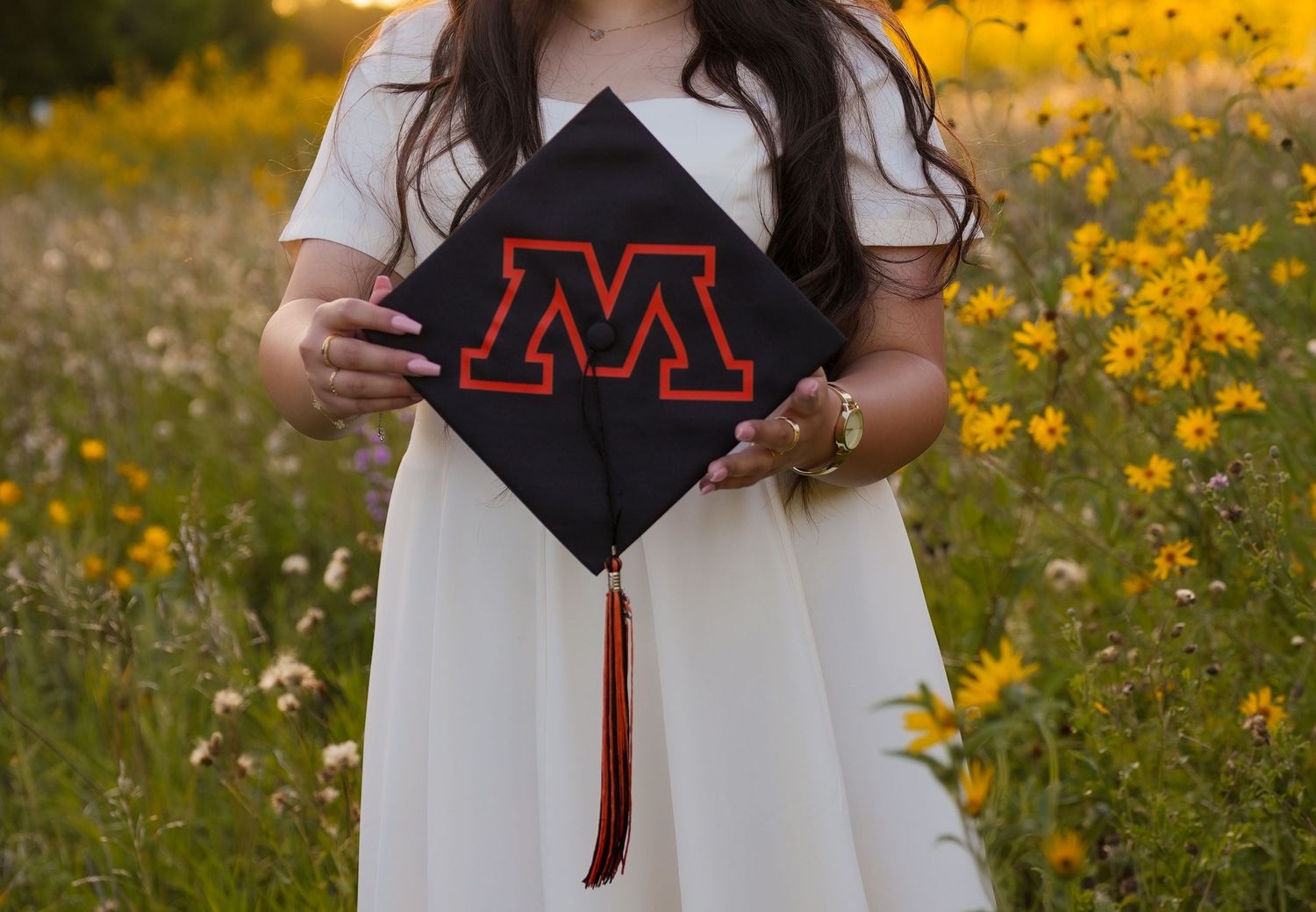 Graduation cap and tassel details against a backdrop of yellow wildflowers.