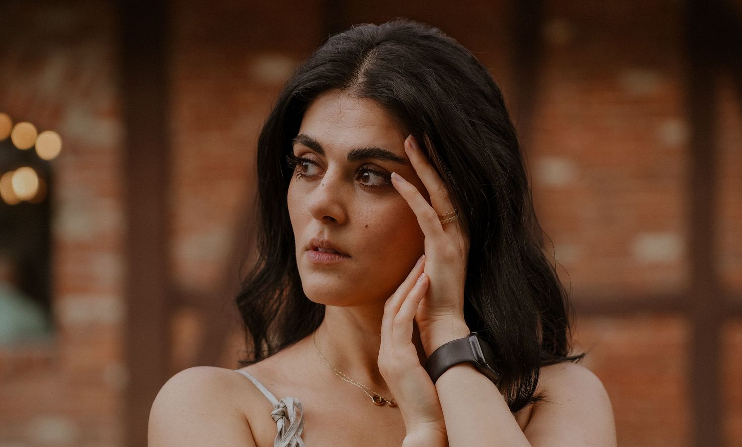 Portrait of someone with dark hair against a brick wall with soft lighting.