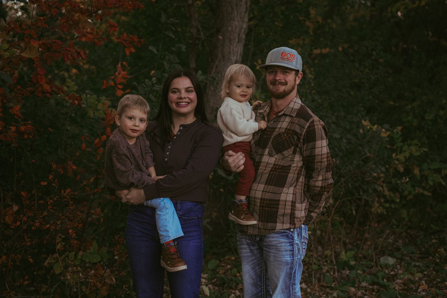Family group stands together among fall foliage wearing casual clothing.