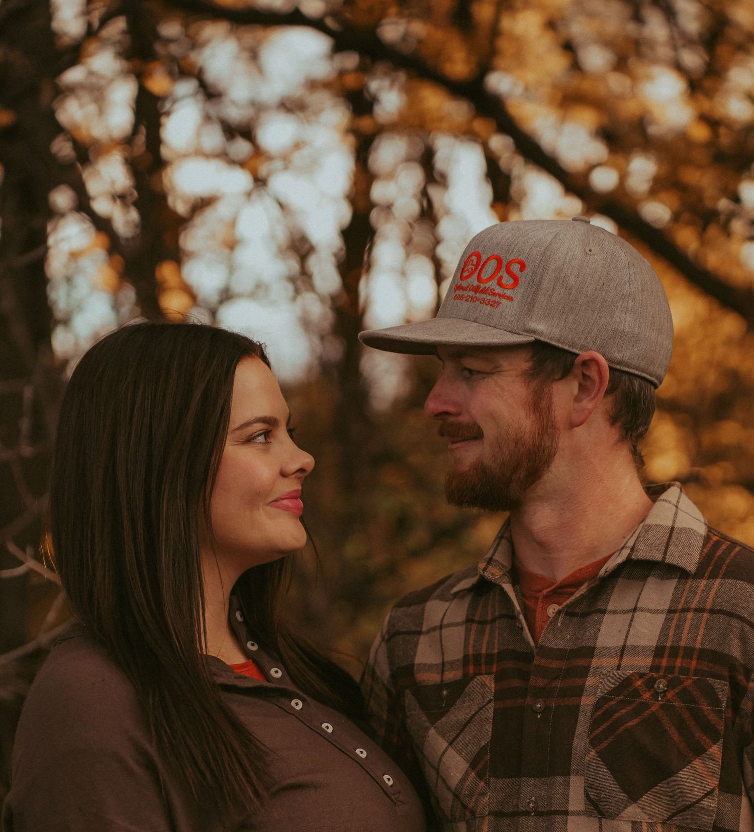 Couple shares intimate moment in autumn woods with golden light filtering through trees.