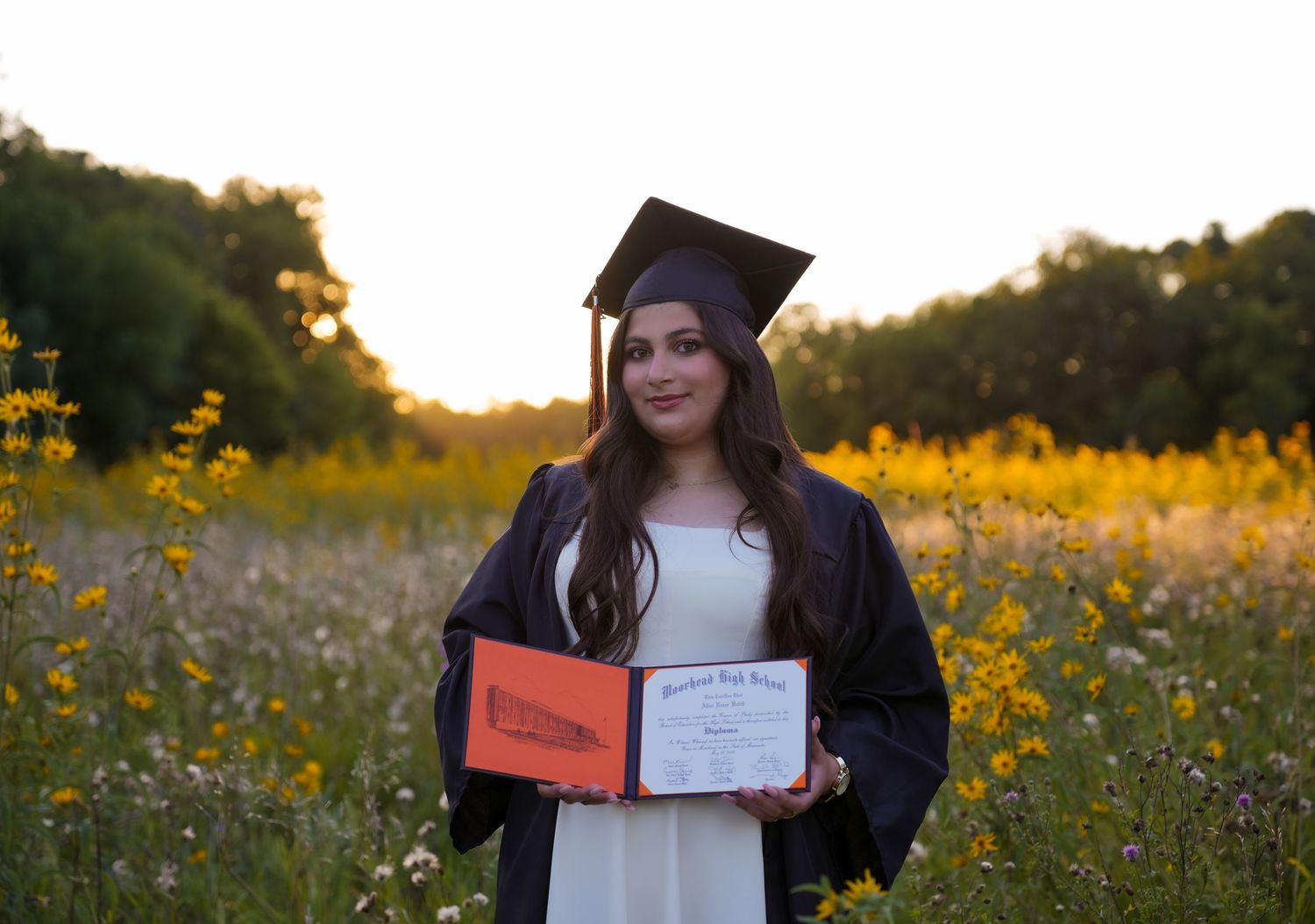 Graduation photos taken in a field of yellow and white wildflowers at sunset.