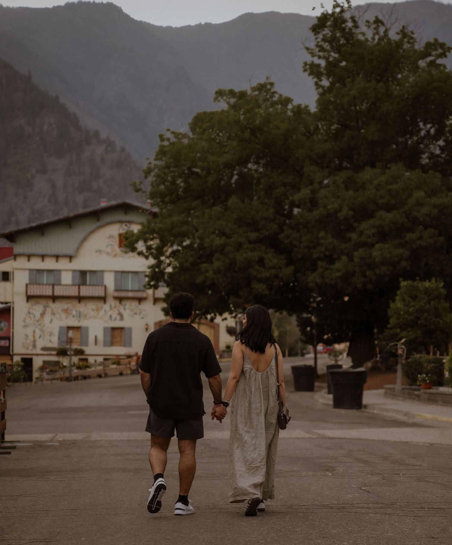 Couple walking hand in hand through a town with mountains in the background.