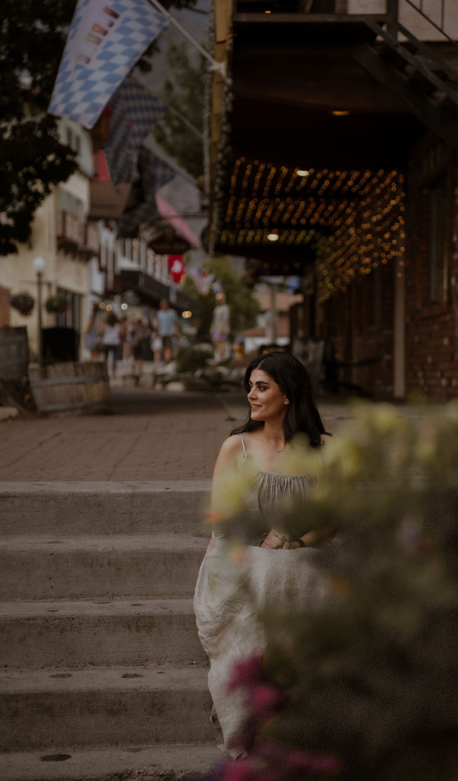 Person in gray dress poses outdoors with decorative flags and string lights in background.