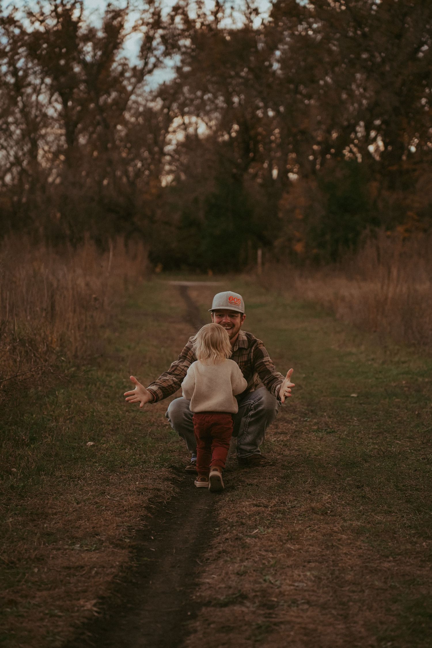 Adult and child share a playful moment on a nature trail at sunset.