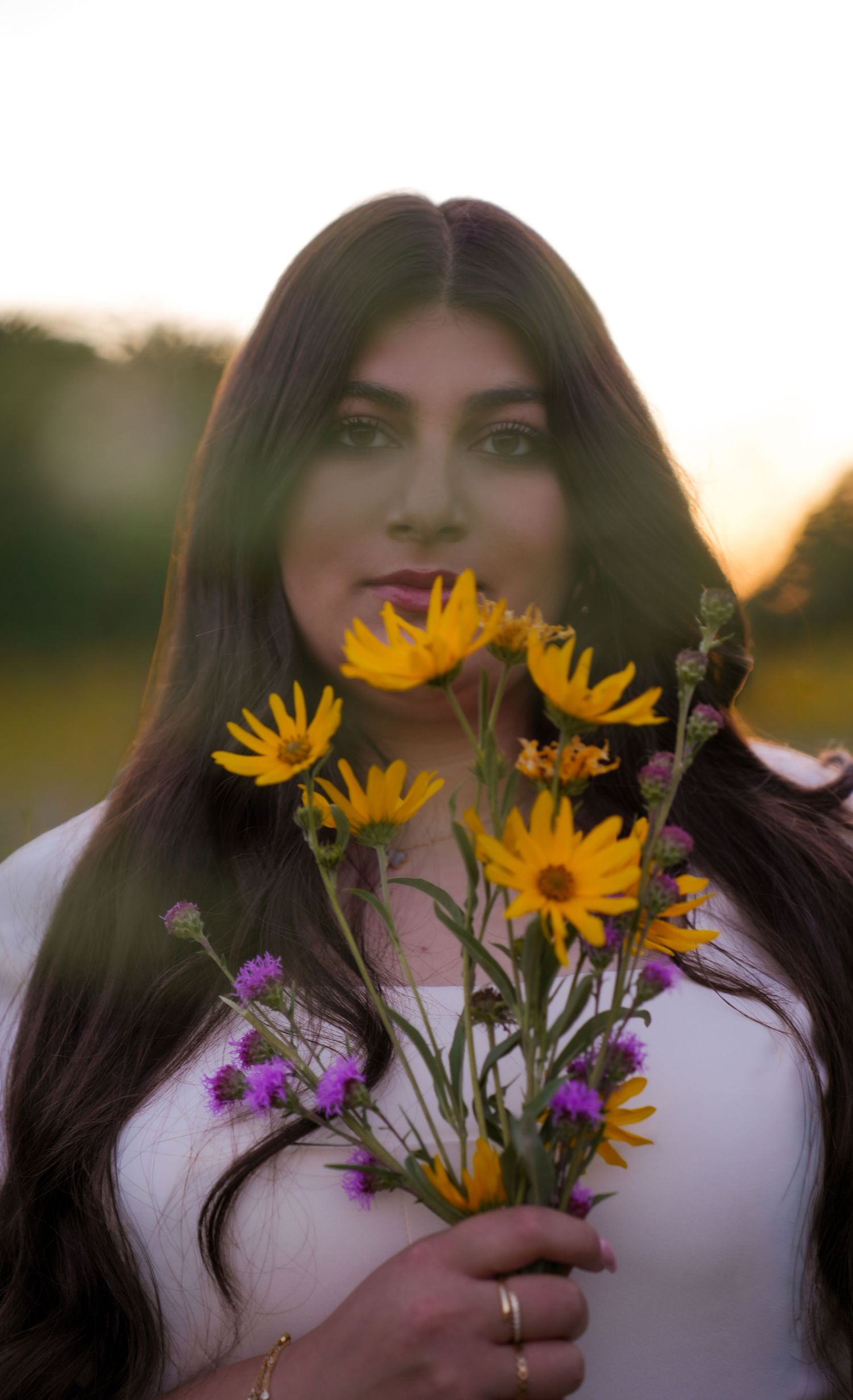 A person holding purple and yellow wildflowers in a sunlit meadow.