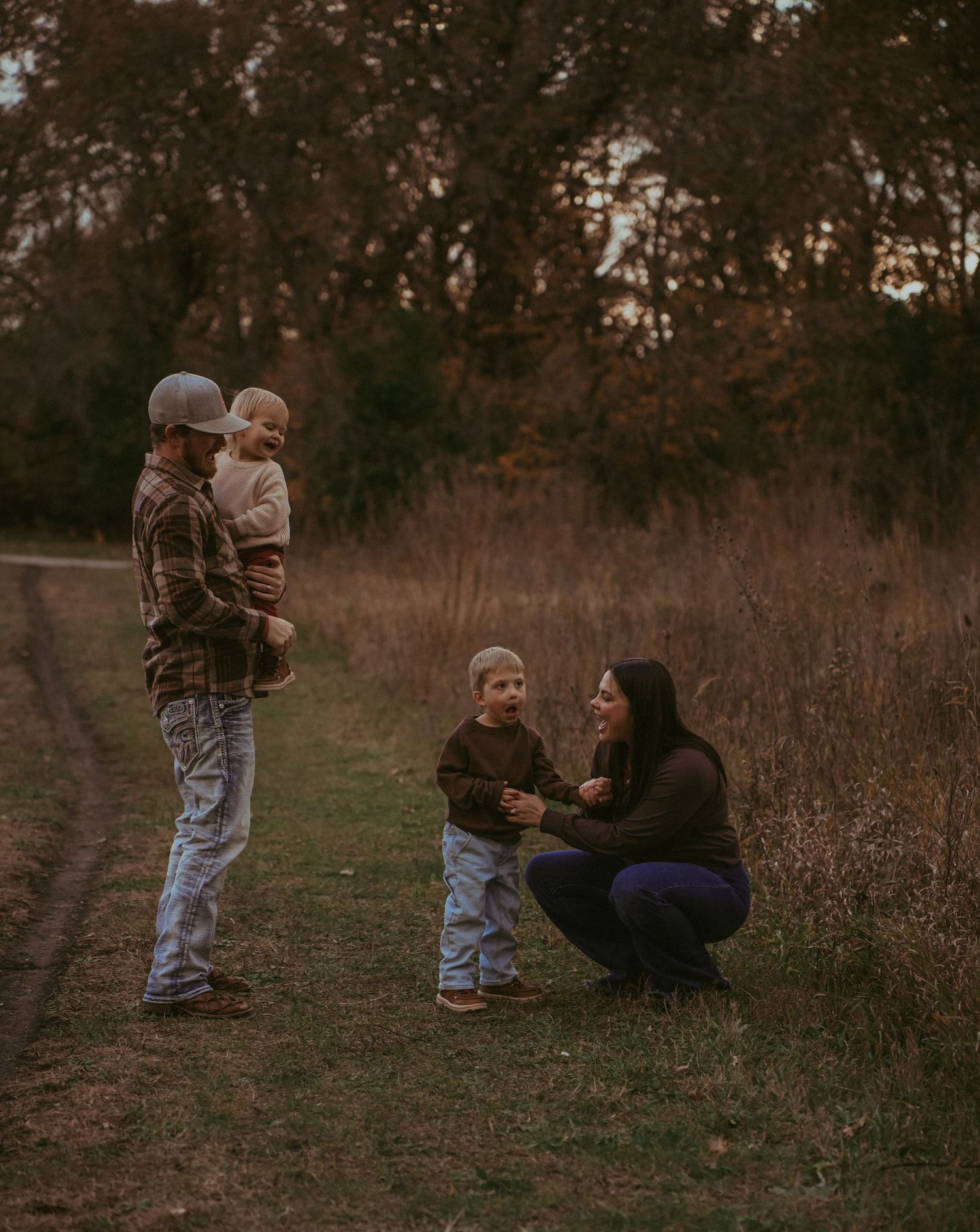 Family members sitting and playing together on a grassy path during sunset.
