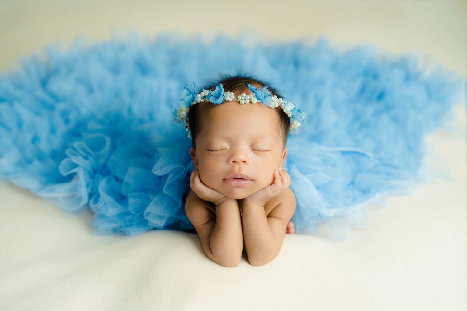 Four soft blue petals with a sleeping newborn baby in each, artistically arranged in a row with white background.