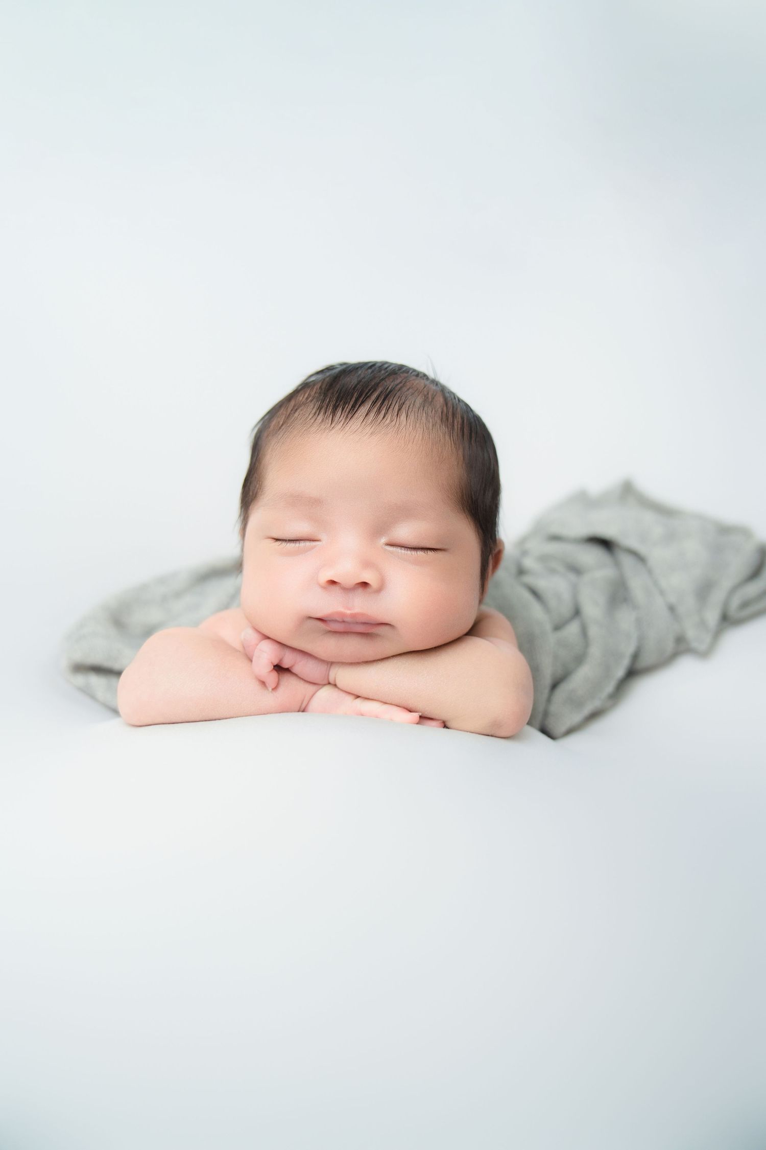 Sleeping newborn with crossed arms resting on white backdrop with gray wrap.