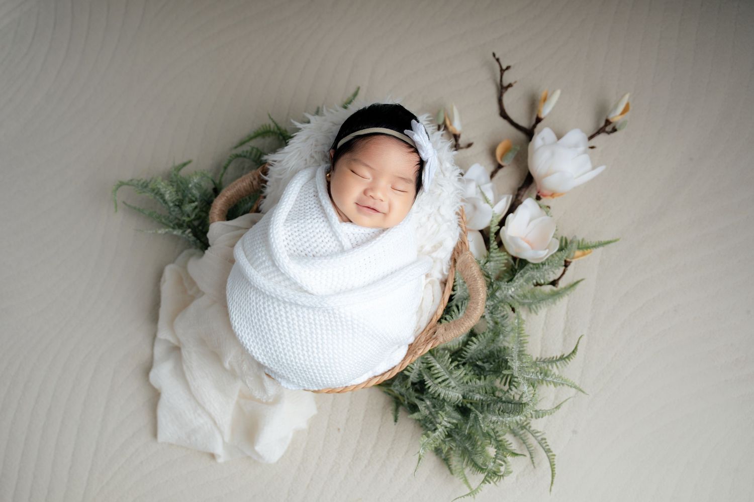 Sleeping newborn wrapped in white blanket lies peacefully among cotton branches and evergreen sprigs.