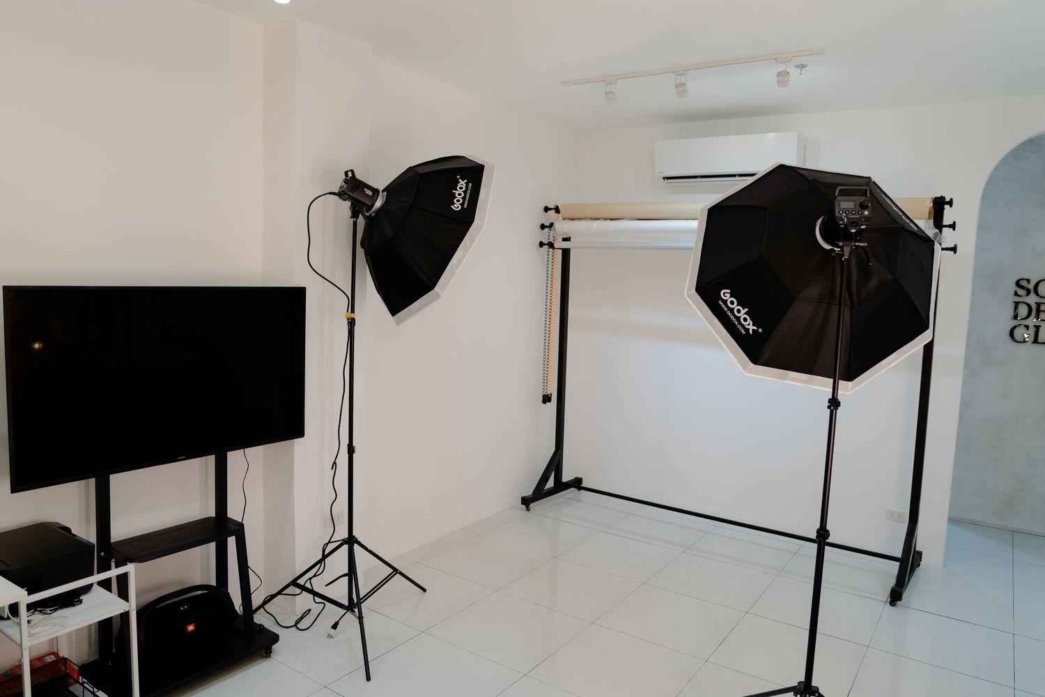 Photography studio setup with black umbrellas, lighting equipment, and white backdrop stand.