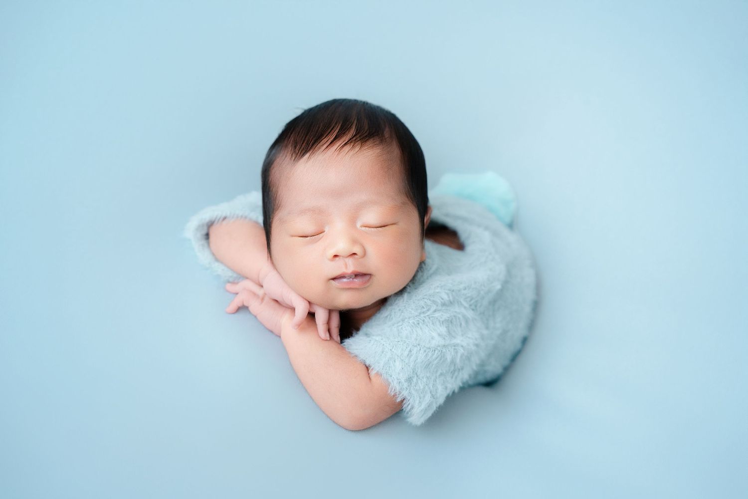 Peaceful newborn resting on light blue blanket during professional photo shoot.