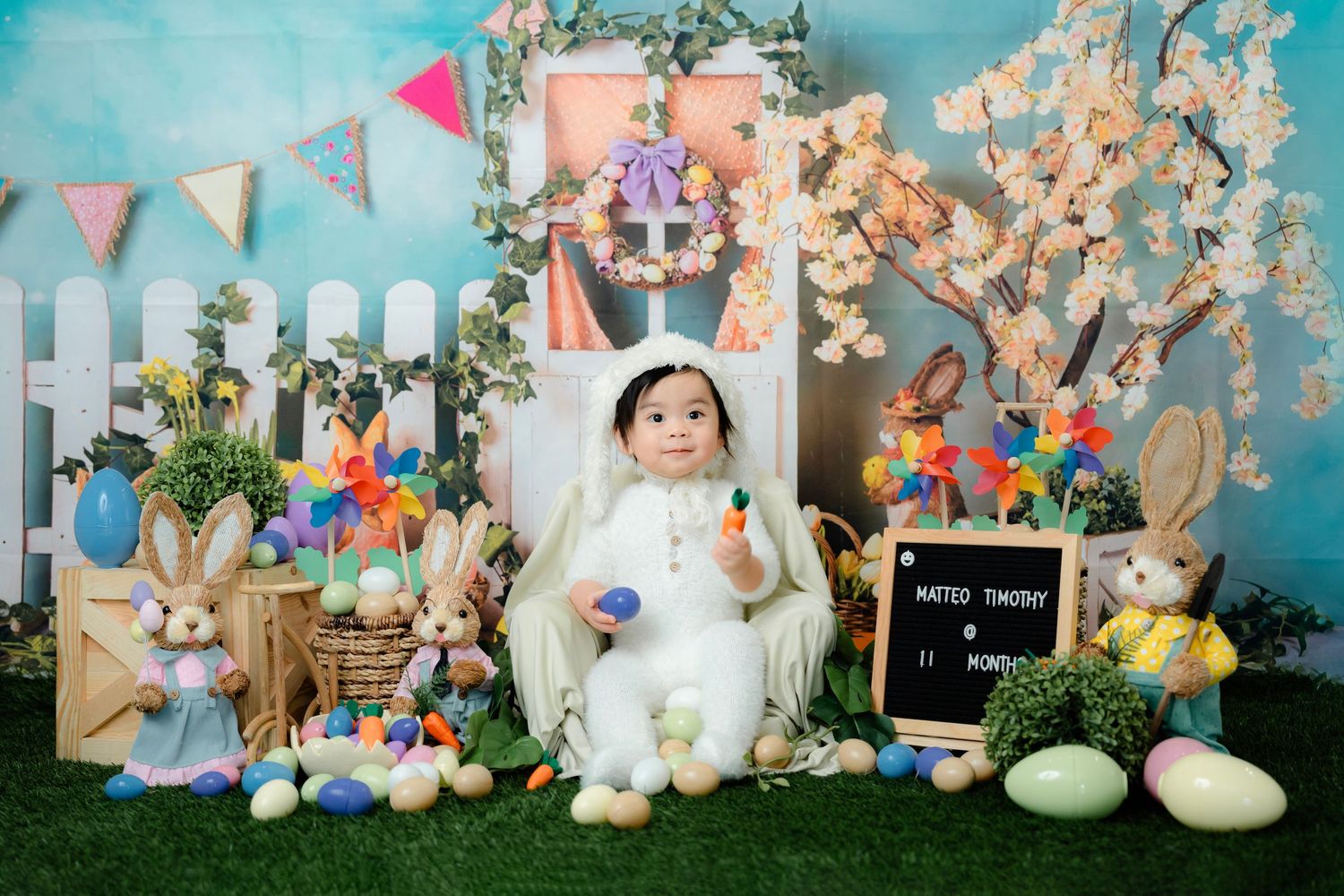 Easter themed photo setup with bunnies, pastel decorations, and spring flowers against blue backdrop.