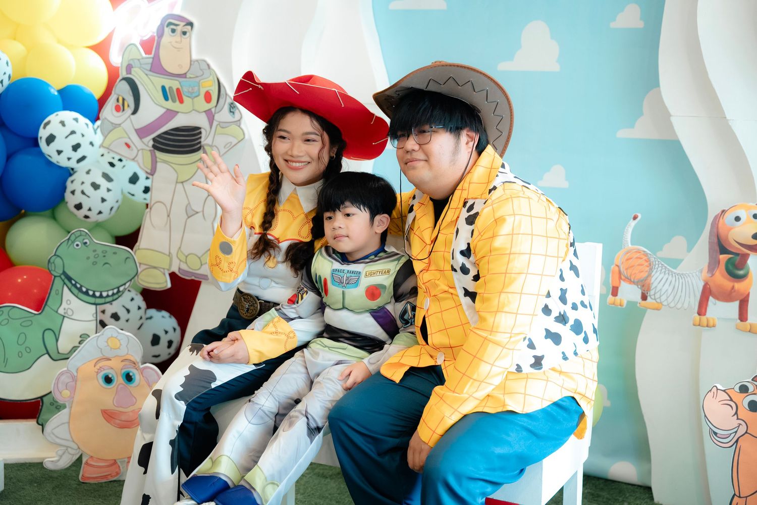 Family dressed in Toy Story costumes posing in front of a colorful Toy Story themed backdrop with balloons.